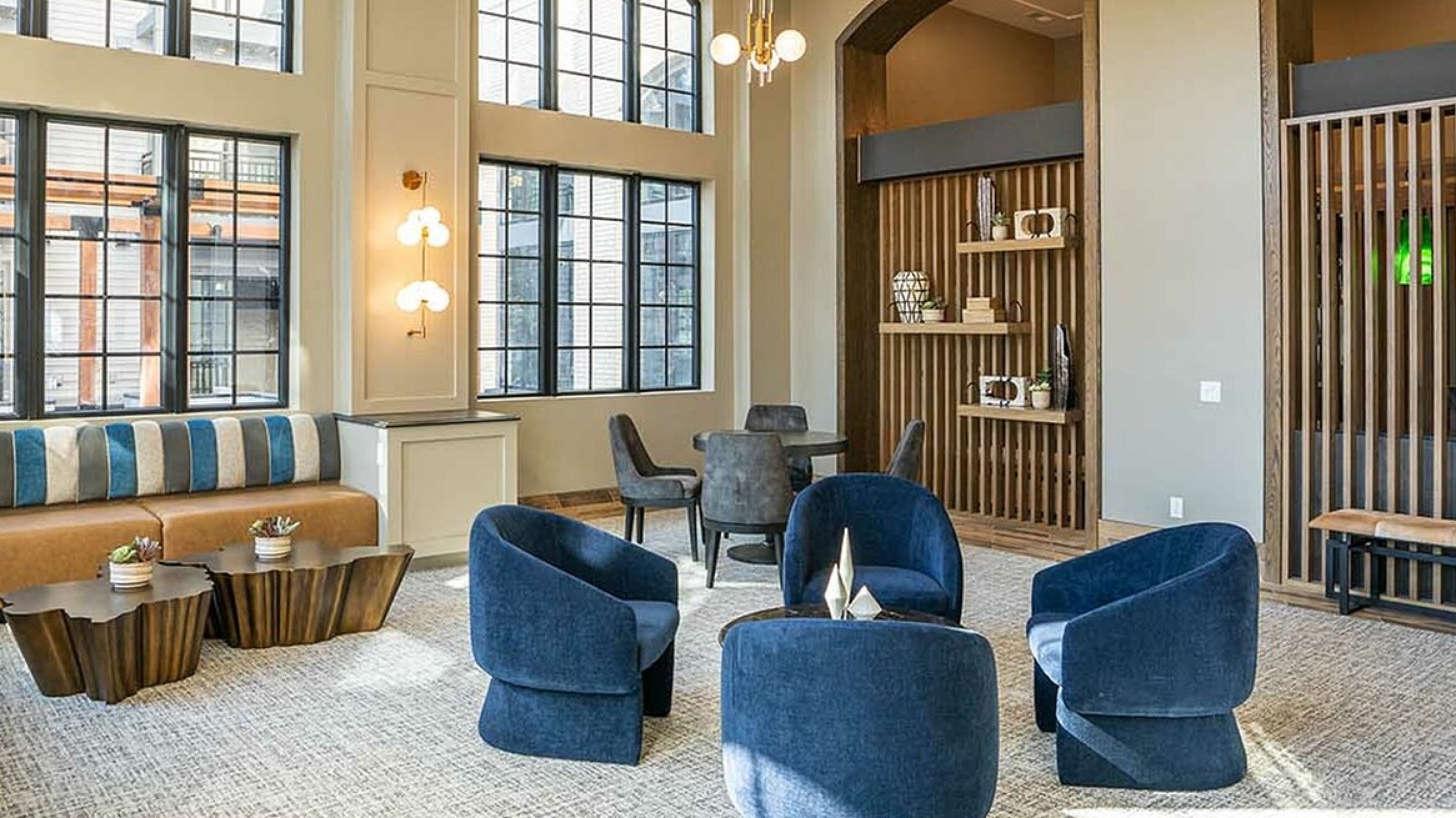 Spacious lounge with modern decor, featuring plush blue chairs, stylish lighting, and large windows.