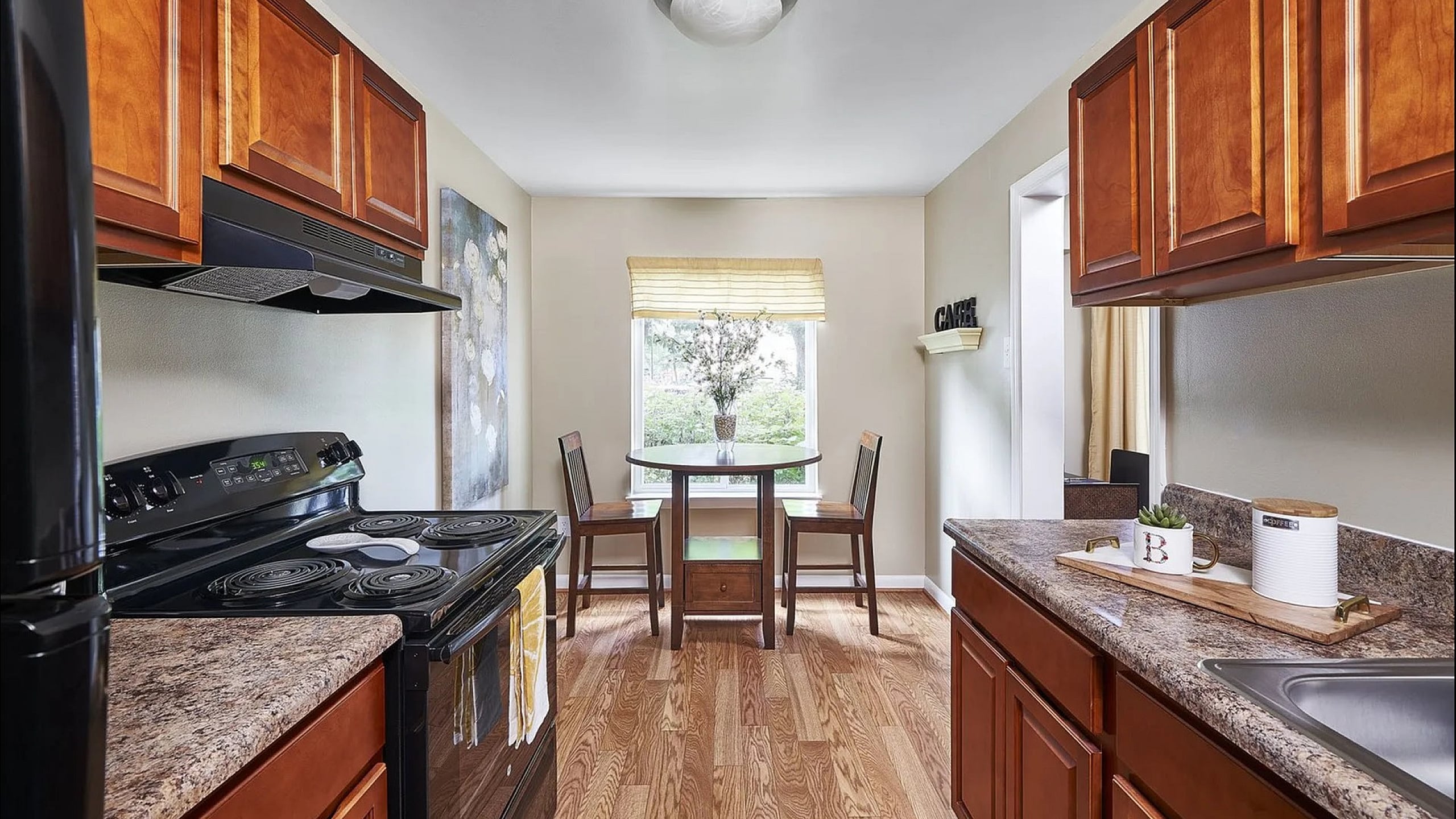Bright and inviting kitchen with rich wooden cabinetry, marble countertops, and a cozy dining nook overlooking lush greenery.