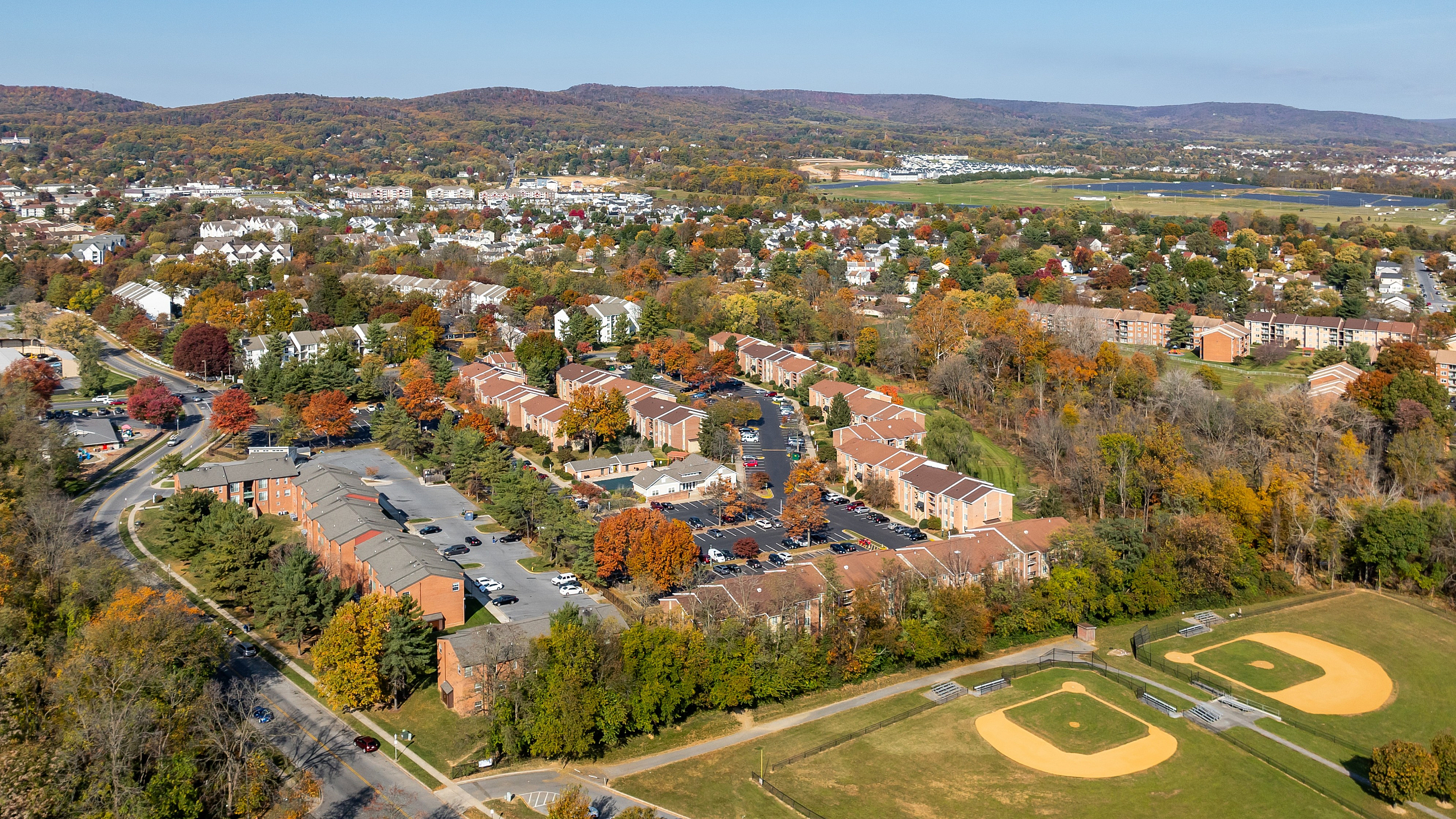 Scenic aerial view of charming suburban neighborhood with vibrant autumn foliage, nestled alongside lush parks and well-designed sports fields.