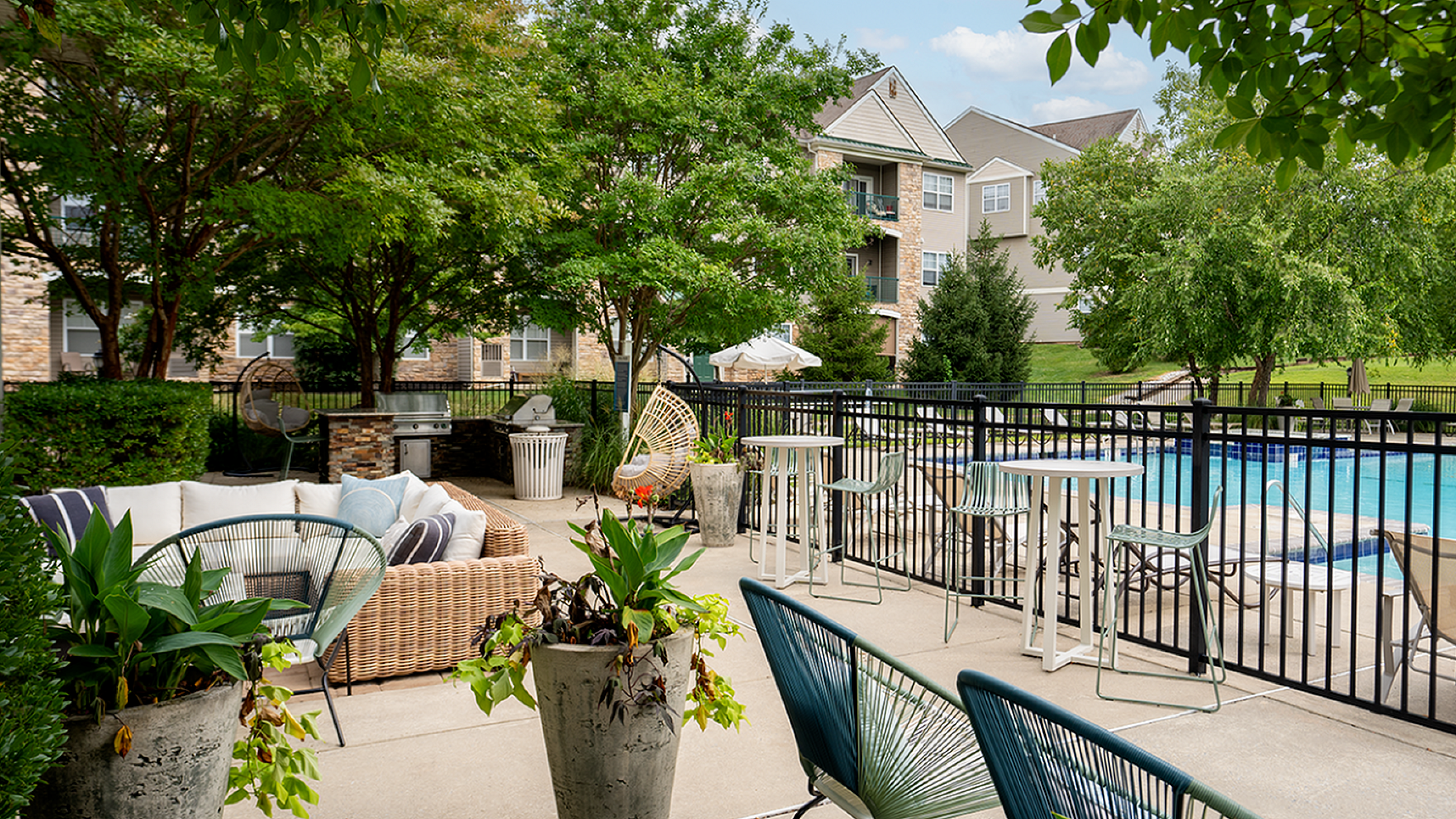 Inviting outdoor patio with lush greenery, modern seating, and poolside view in a serene apartment setting.
