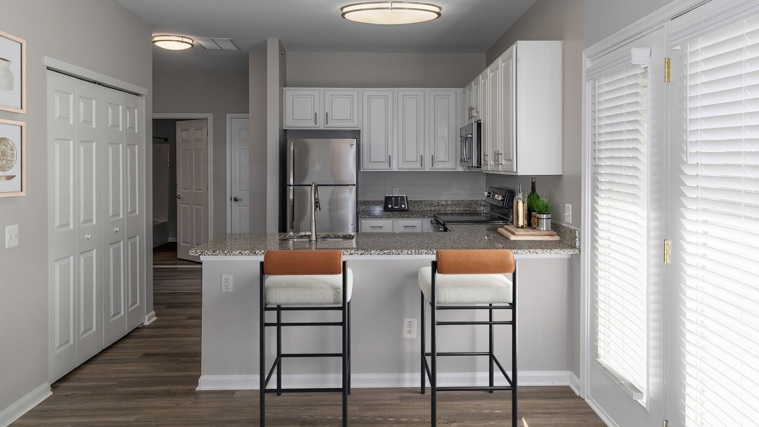 Modern kitchen with sleek granite countertops, stainless steel appliances, and chic bar stools, illuminated by natural light.