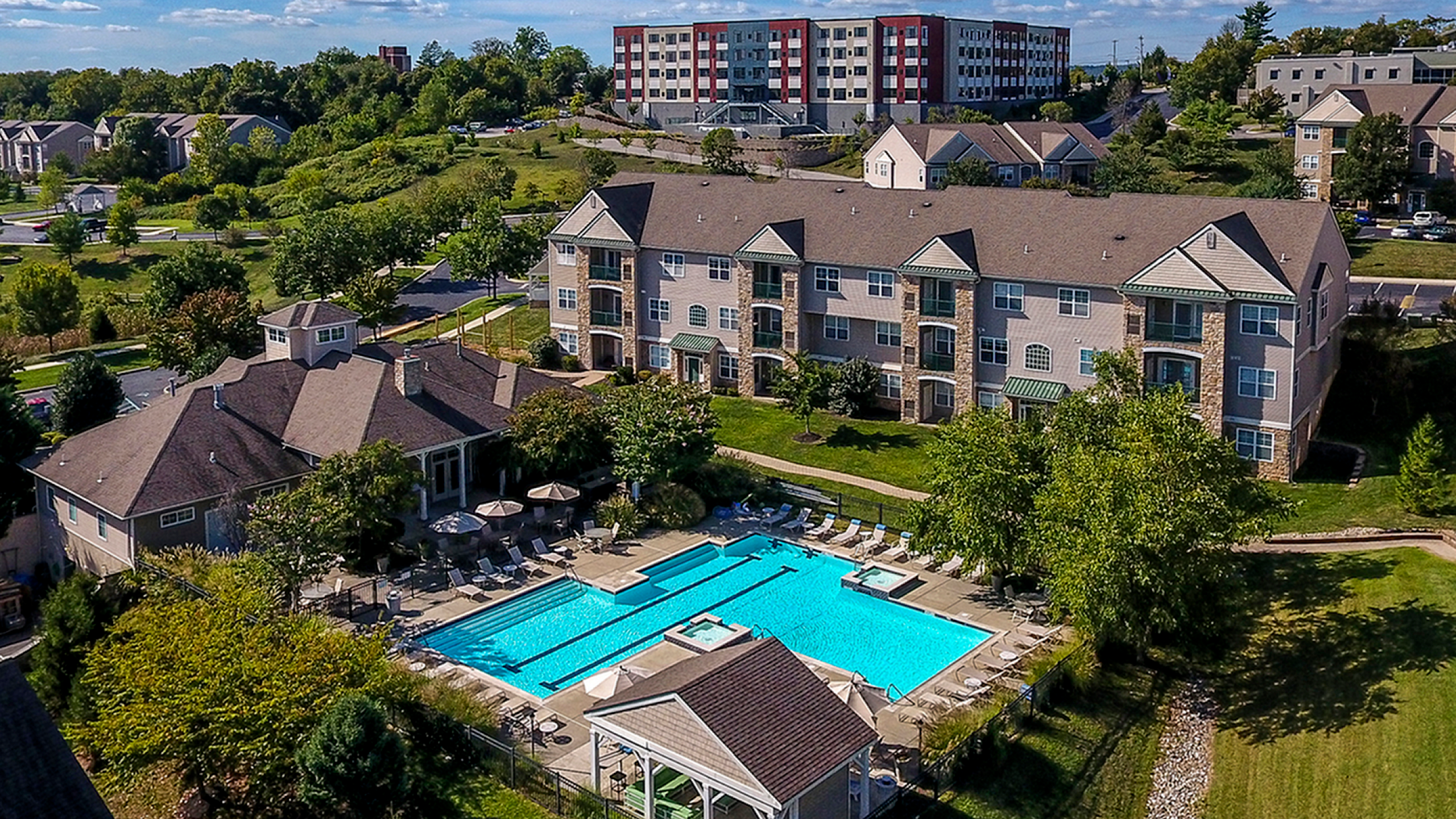 Stunning aerial view of a serene apartment complex featuring a sparkling pool, lush greenery, and spacious living areas.