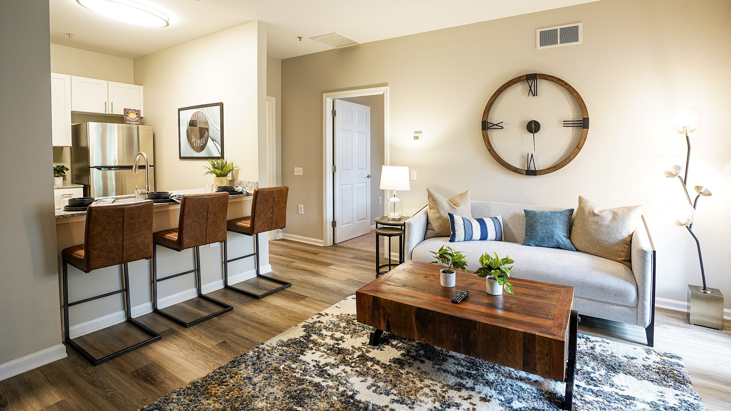 Modern living room with elegant decor, featuring a cozy sofa, rustic wooden coffee table, stylish bar stools, and contemporary kitchen in open-concept design.