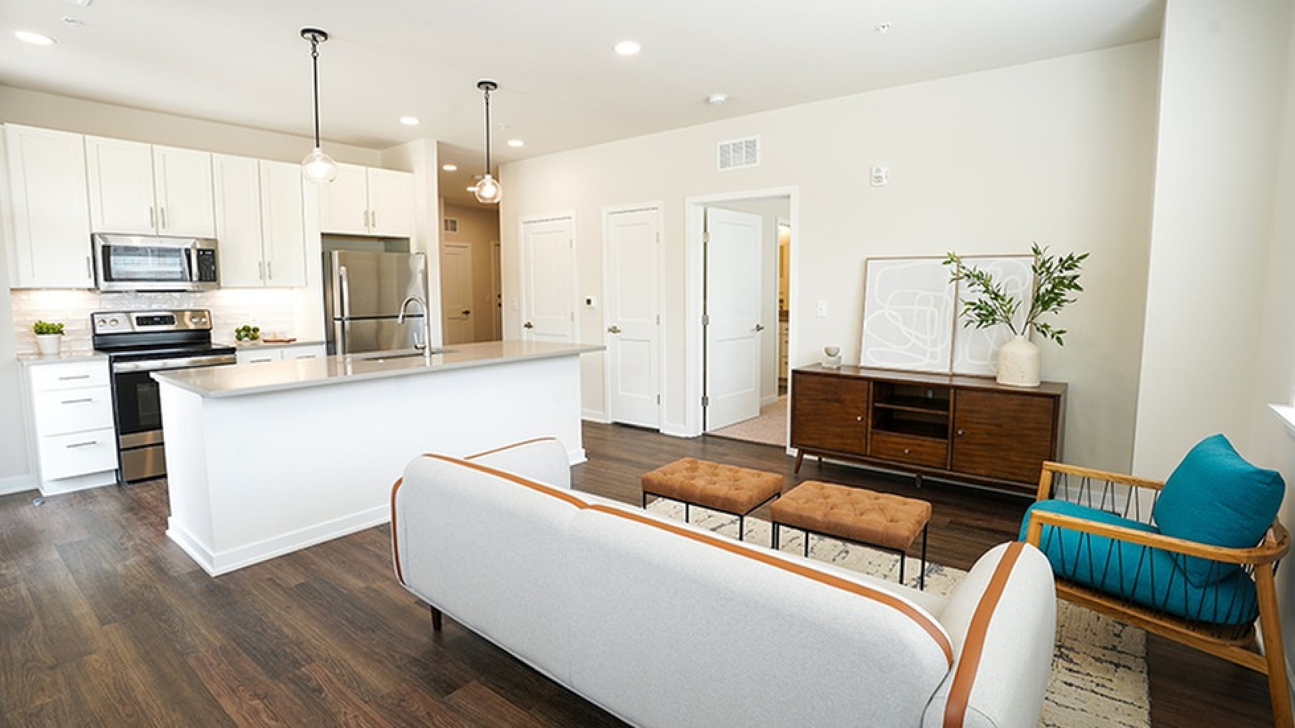 Modern open-concept living space featuring a sleek kitchen with white cabinets and stainless steel appliances, cozy seating area, and stylish decor.