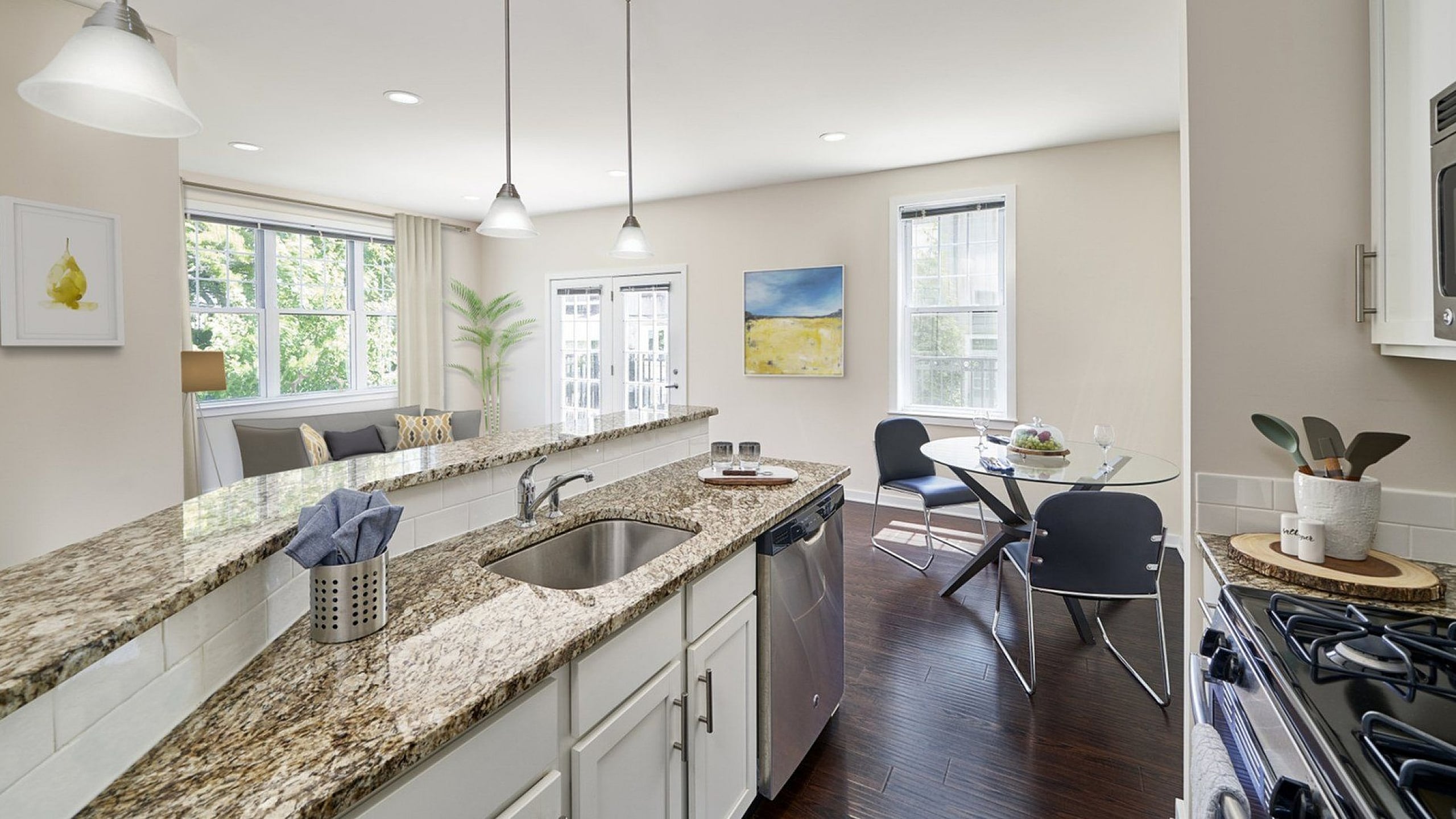 Bright and modern apartment kitchen with granite countertops, pendant lighting, and an open-plan dining area.