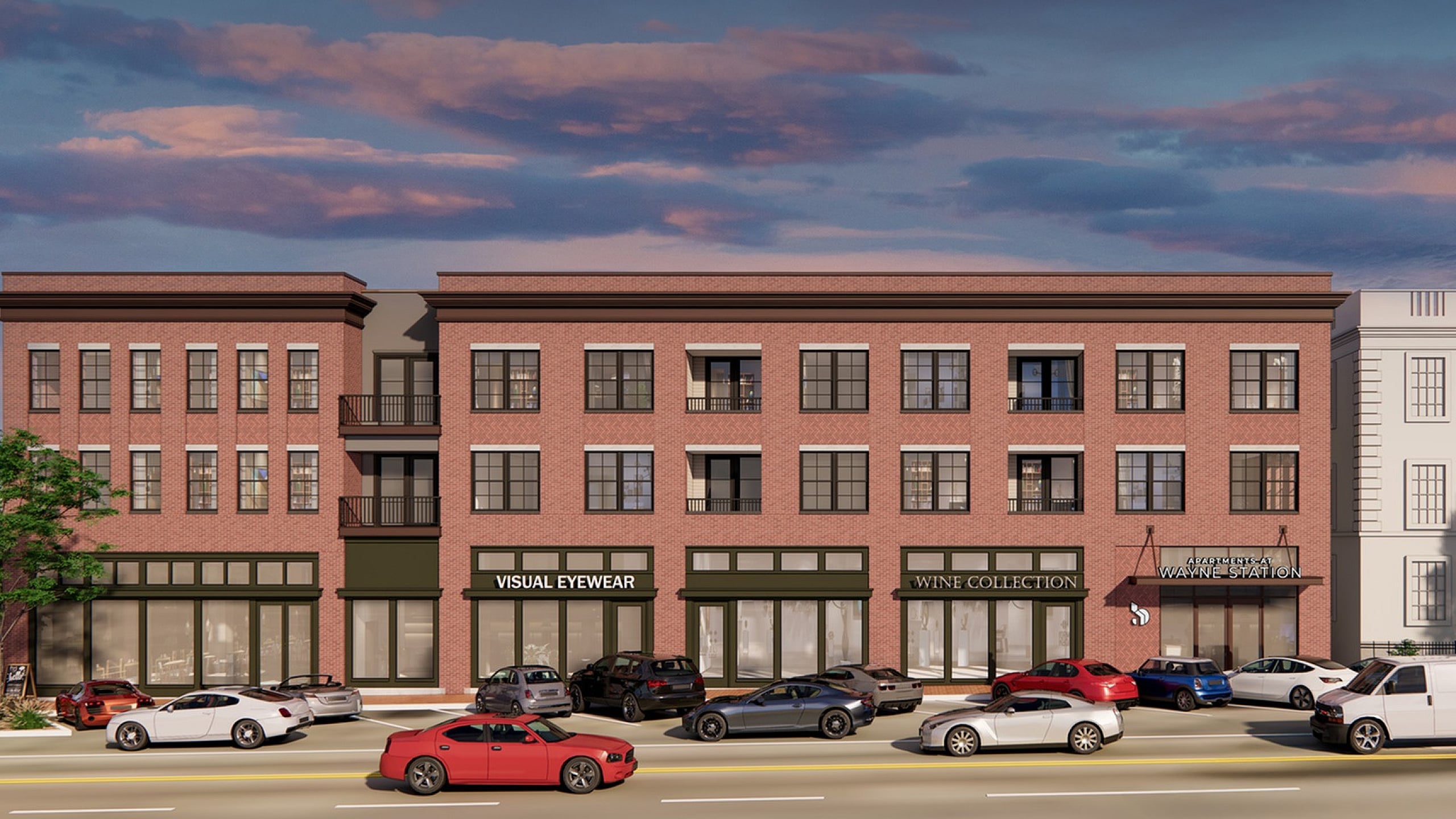 Charming three-story brick building with large windows and vibrant retail spaces, nestled under a picturesque evening sky.