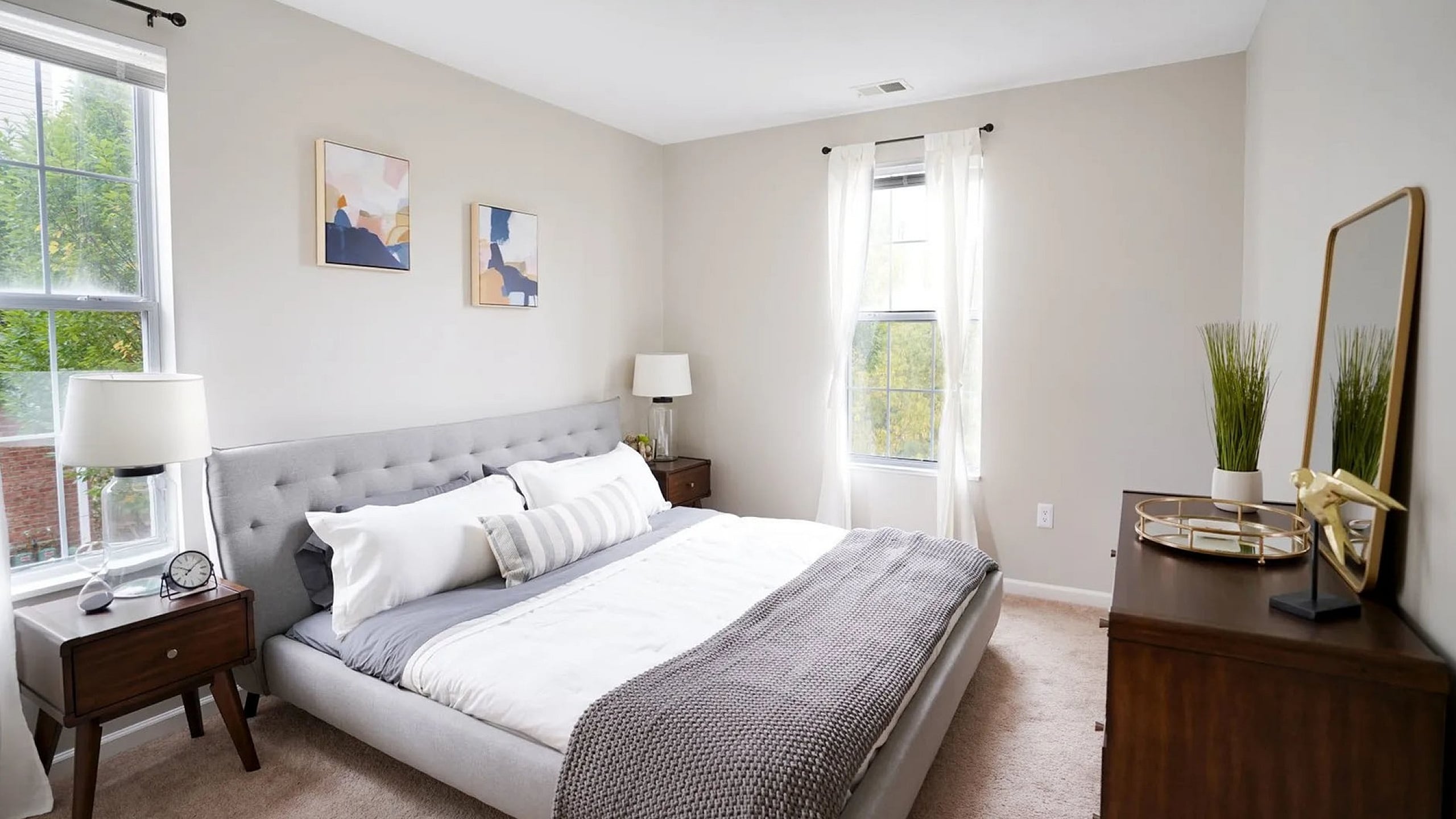 Bright and airy bedroom with a plush gray bed, stylish side tables, and elegant window treatments, perfect for relaxation.
