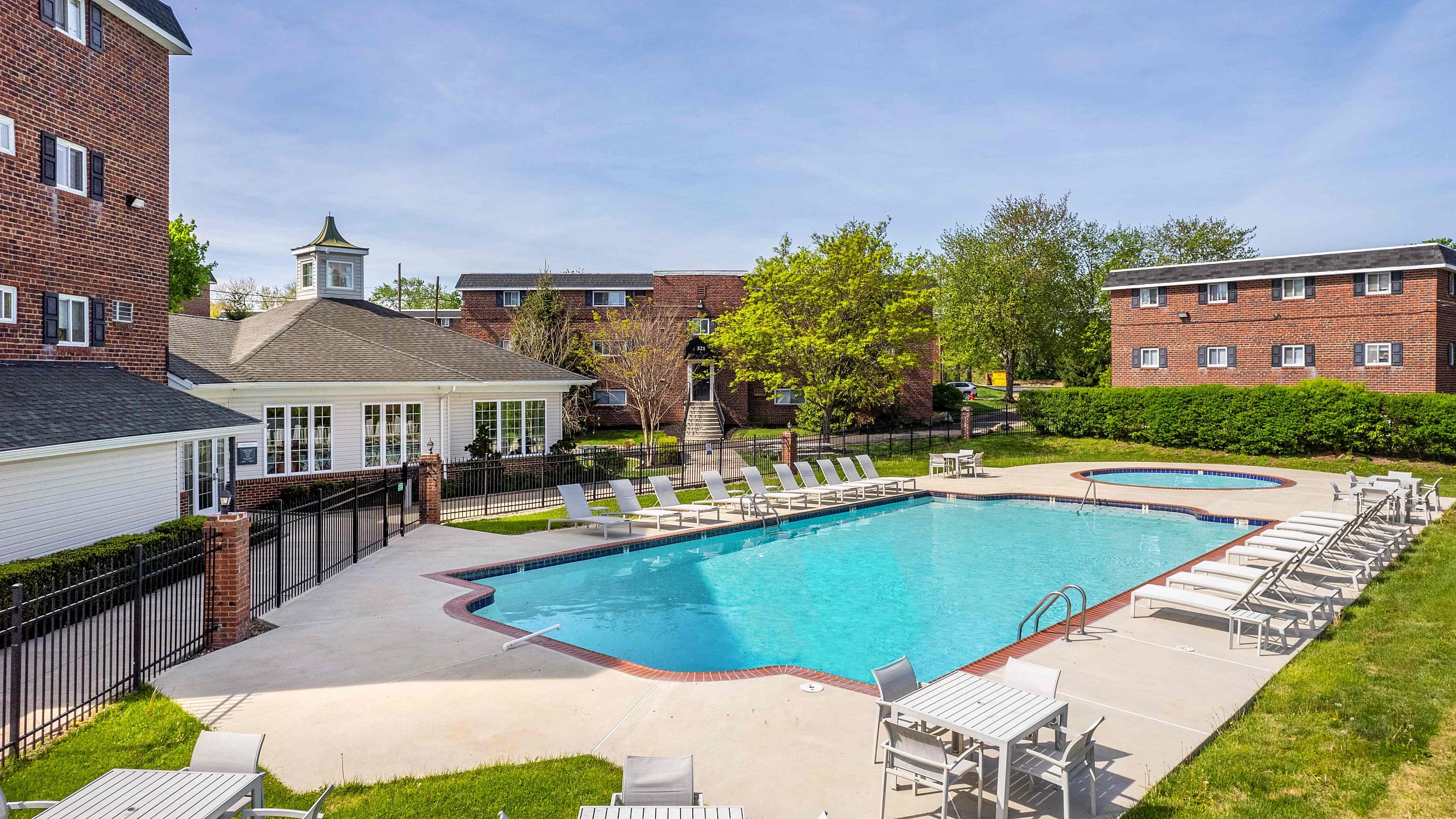 Inviting apartment complex with a sparkling outdoor pool, surrounded by modern lounge chairs and vibrant green landscaping, ideal for relaxation.