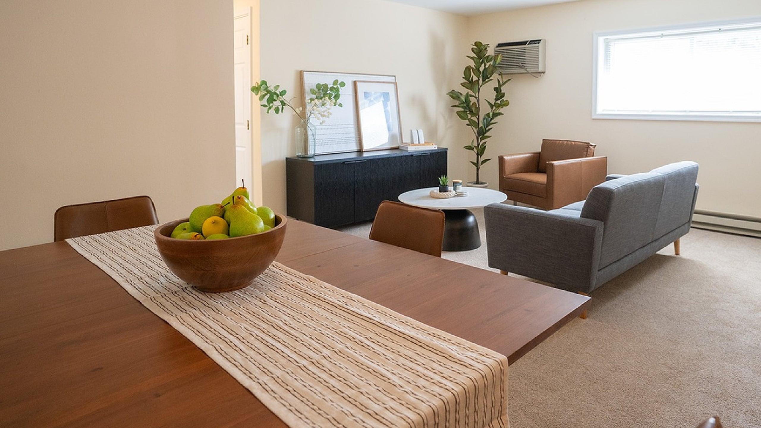 Inviting living room with stylish seating, large window, and cozy dining area with a fruit centerpiece.