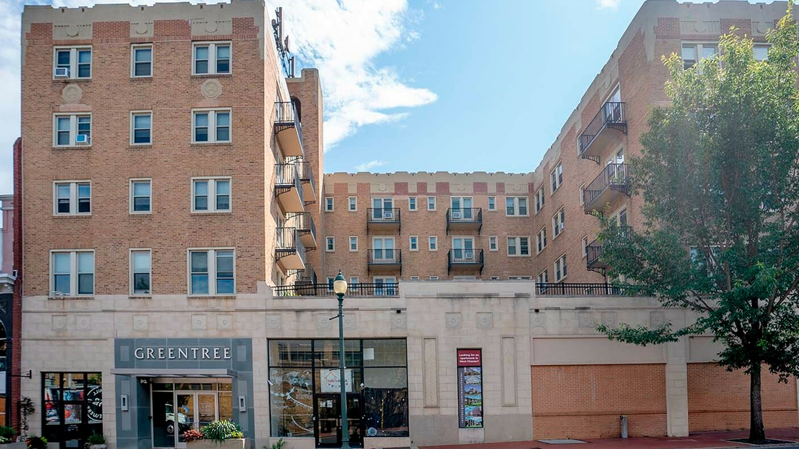 Charming brick apartment complex with a welcoming entrance, set against a bright blue sky.