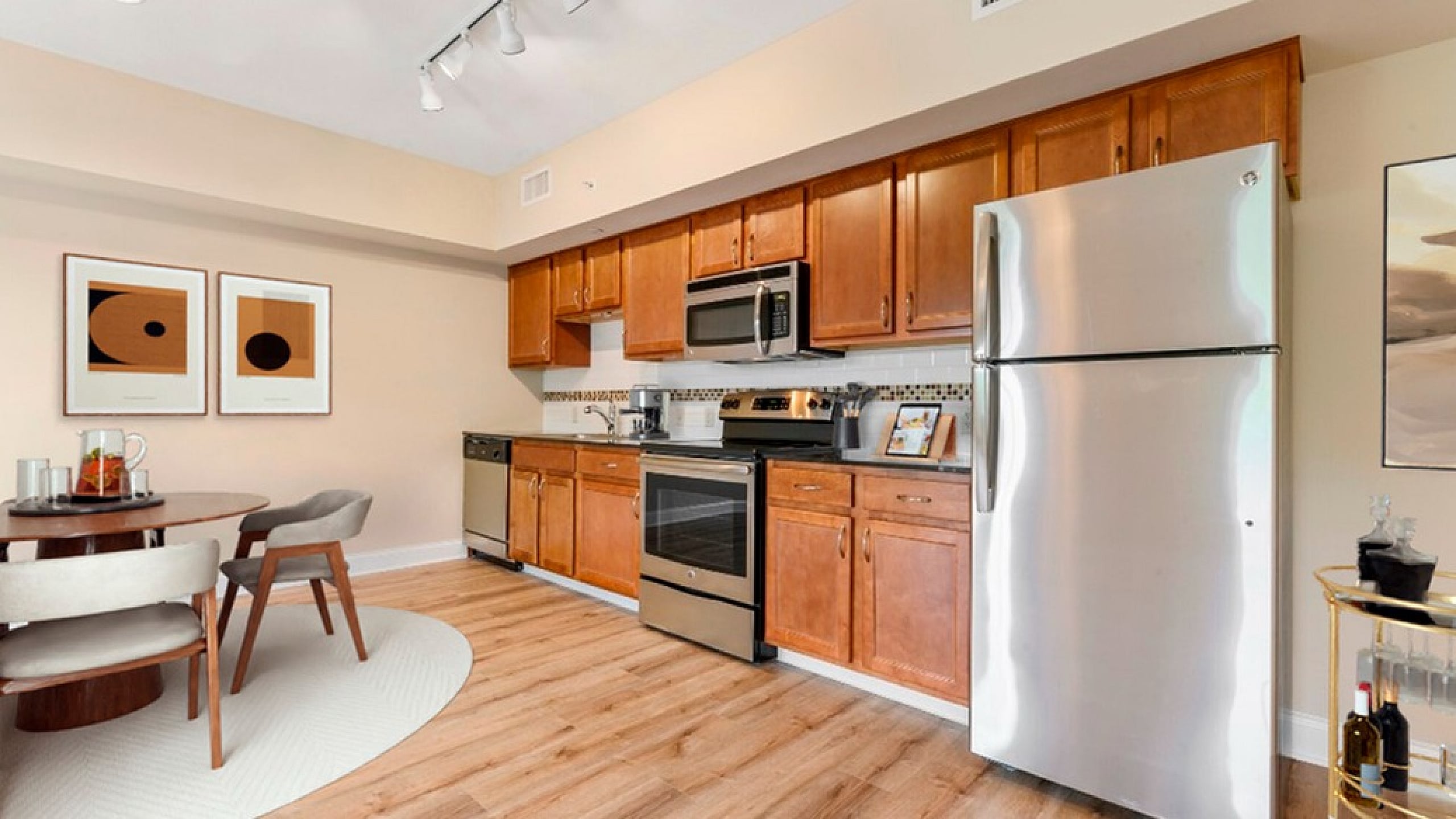 Modern kitchen with stainless steel appliances, warm wooden cabinetry, and a cozy dining area, featuring stylish decor and polished wood flooring.