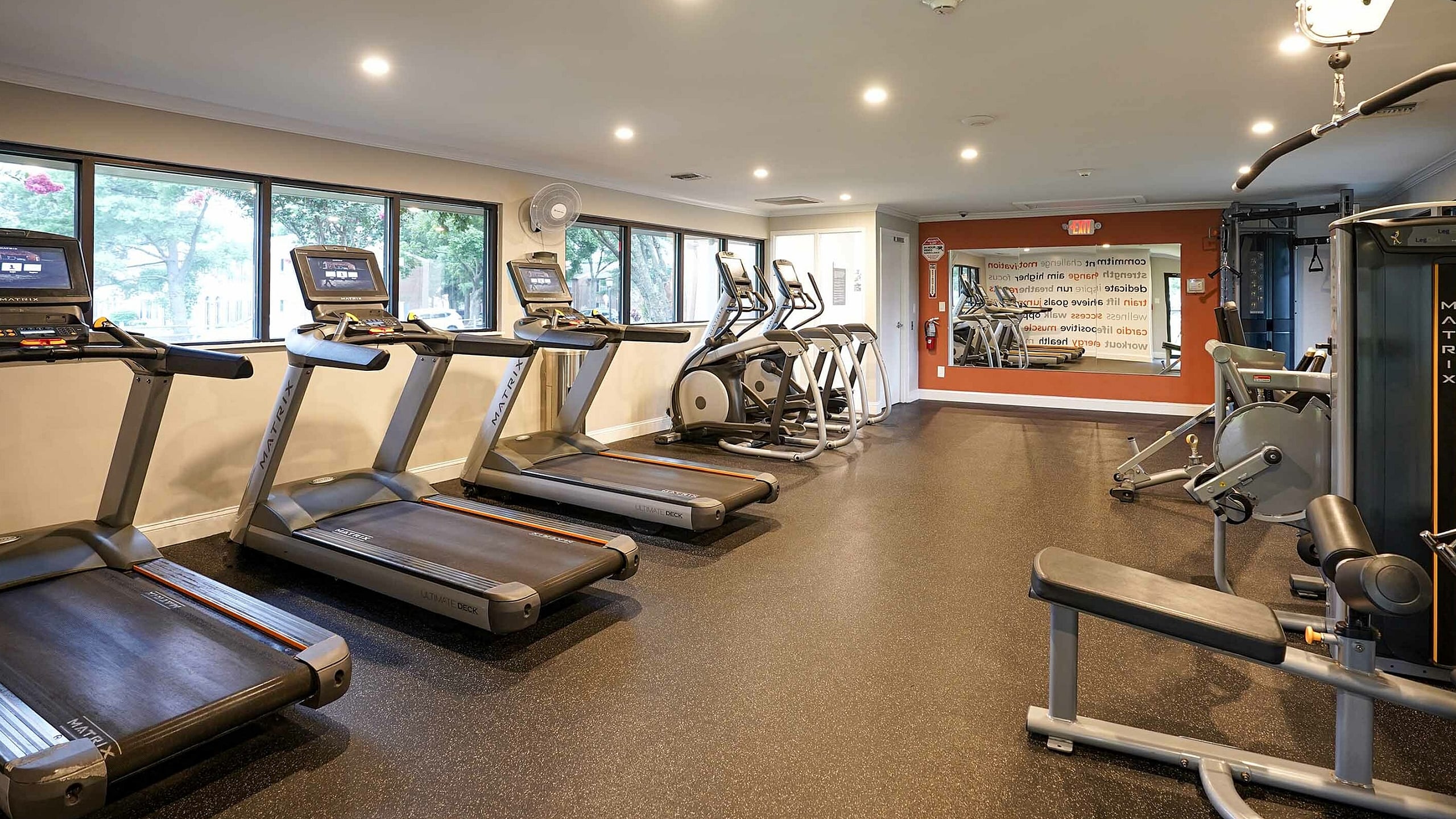 Modern fitness center equipped with state-of-the-art treadmills, elliptical machines, and strength training equipment, featuring large windows and ample natural light.