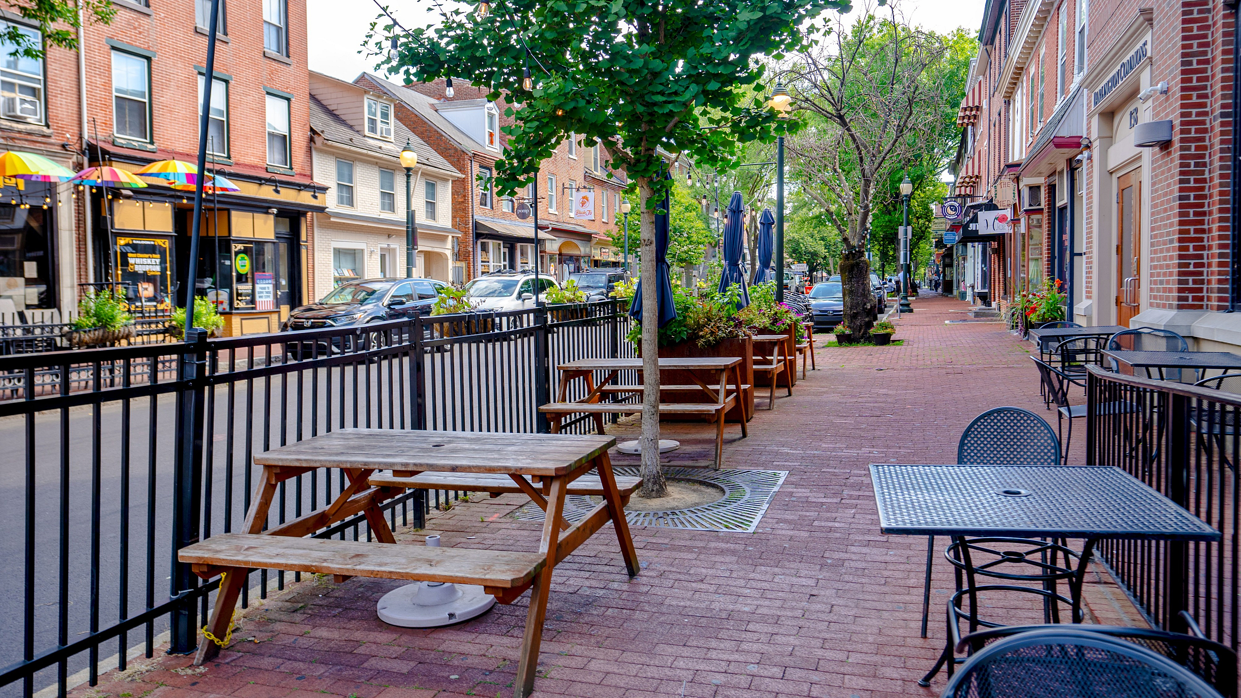 Charming streetscape featuring inviting outdoor seating, vibrant storefronts, and lush greenery, perfect for urban dining and relaxation.