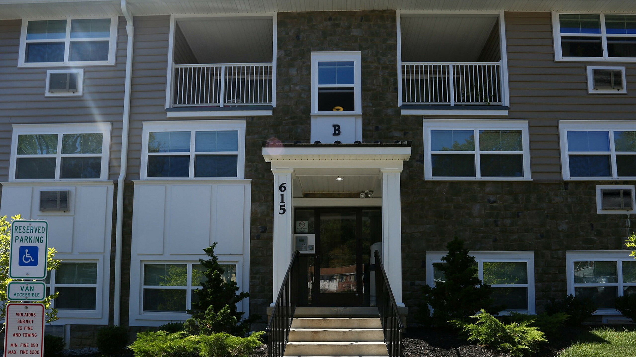 Charming apartment building featuring modern stone facade, lush landscaping, and accessible entry.