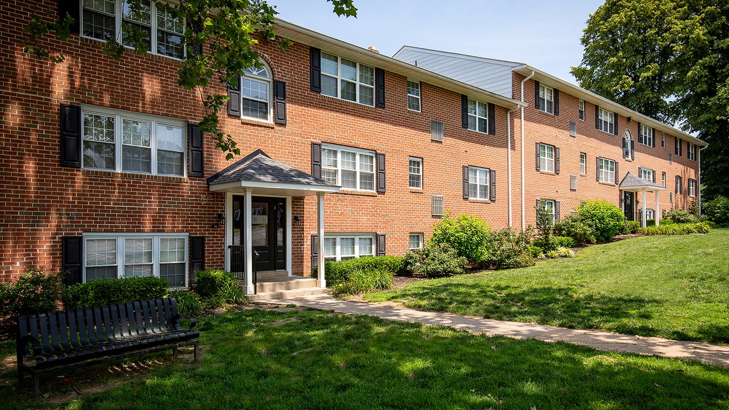 Charming brick apartment building with lush landscaping and inviting entrance, perfect for comfortable suburban living.