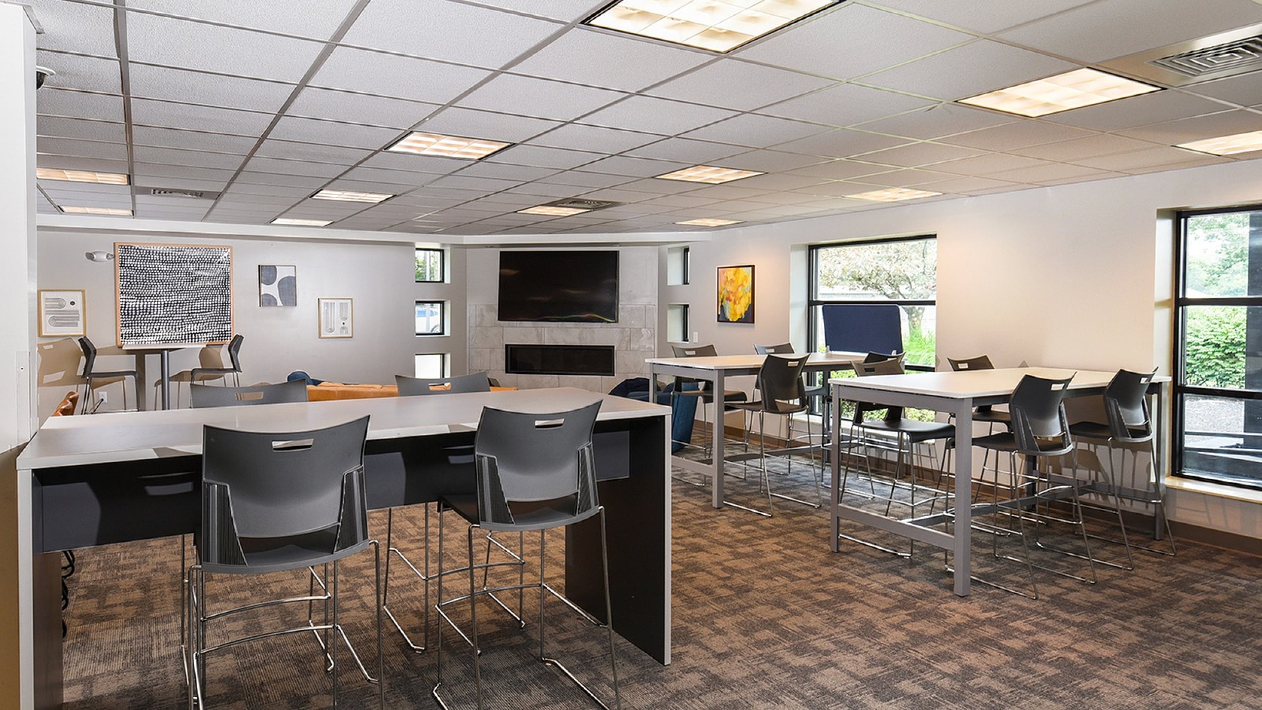 Modern communal space with sleek high-top tables, contemporary chairs, and large windows offering abundant natural light.
