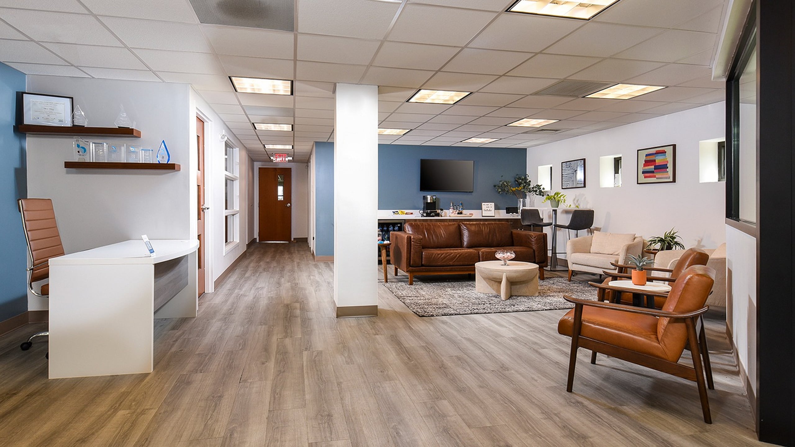Modern office reception area with sleek wooden flooring, comfortable leather seating, stylish decor, and a welcoming ambiance.