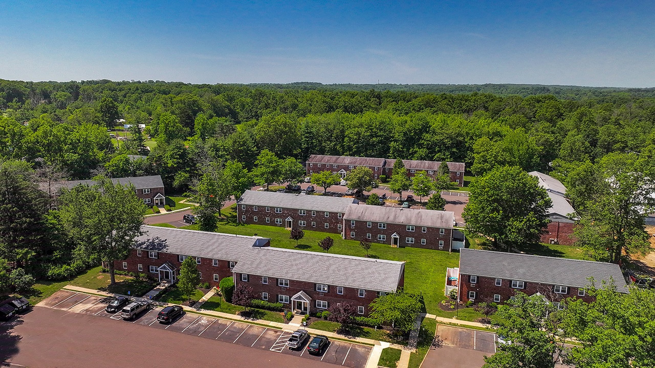 Scenic aerial view of charming brick apartment buildings nestled in lush greenery, offering a peaceful residential setting.