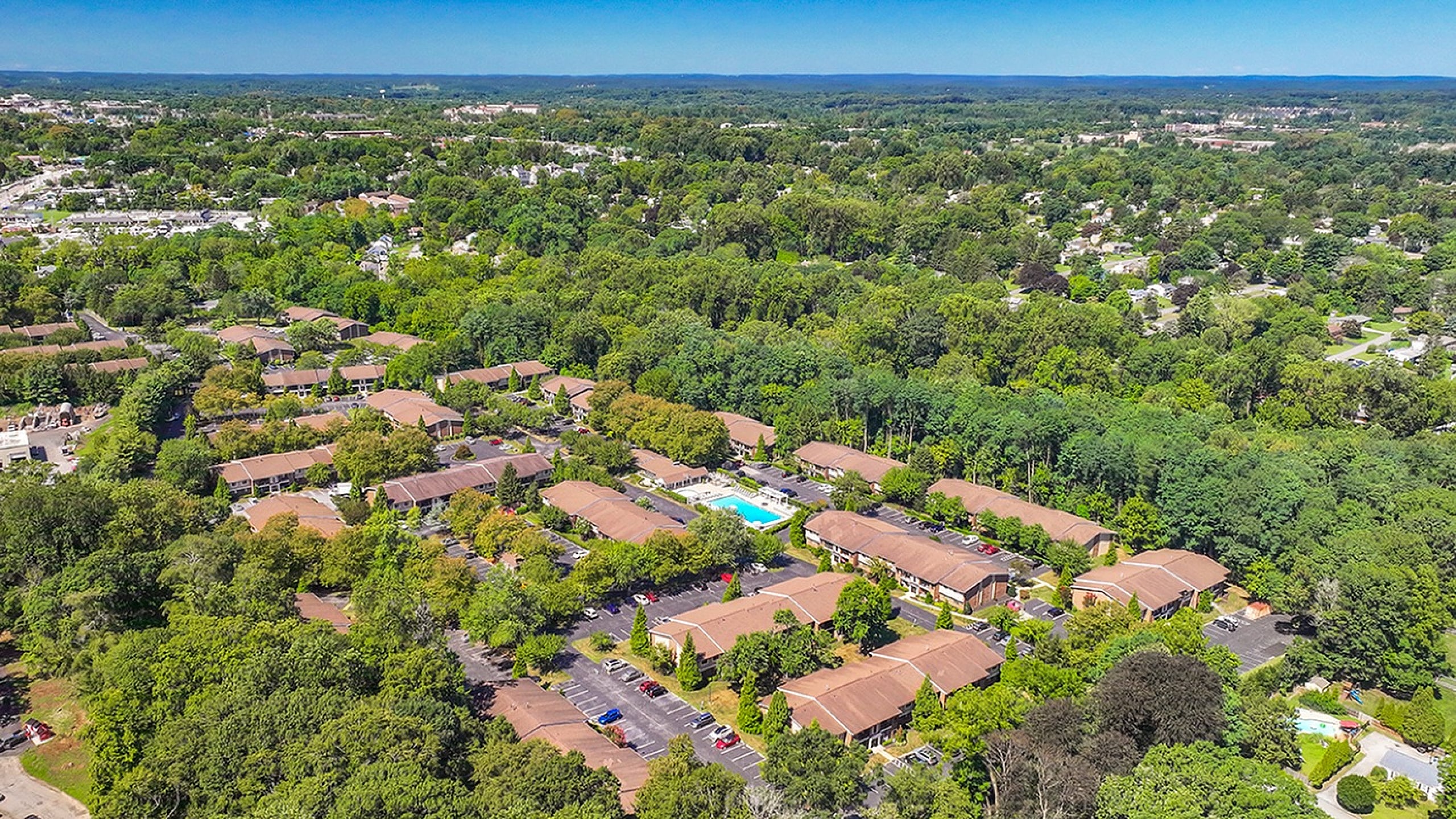 Aerial view of a serene residential complex nestled in lush greenery with modern amenities and a central pool, offering a tranquil suburban lifestyle.