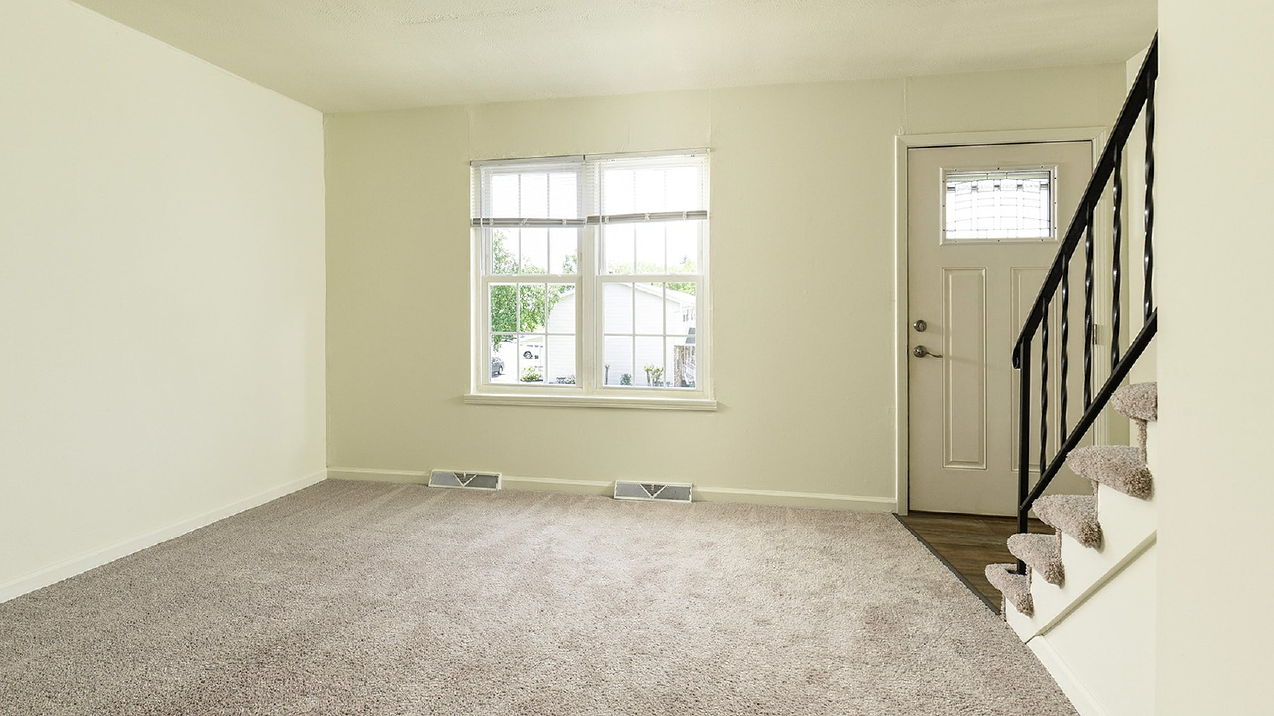 Bright living room with plush carpeting, elegant staircase, and large window inviting natural light.