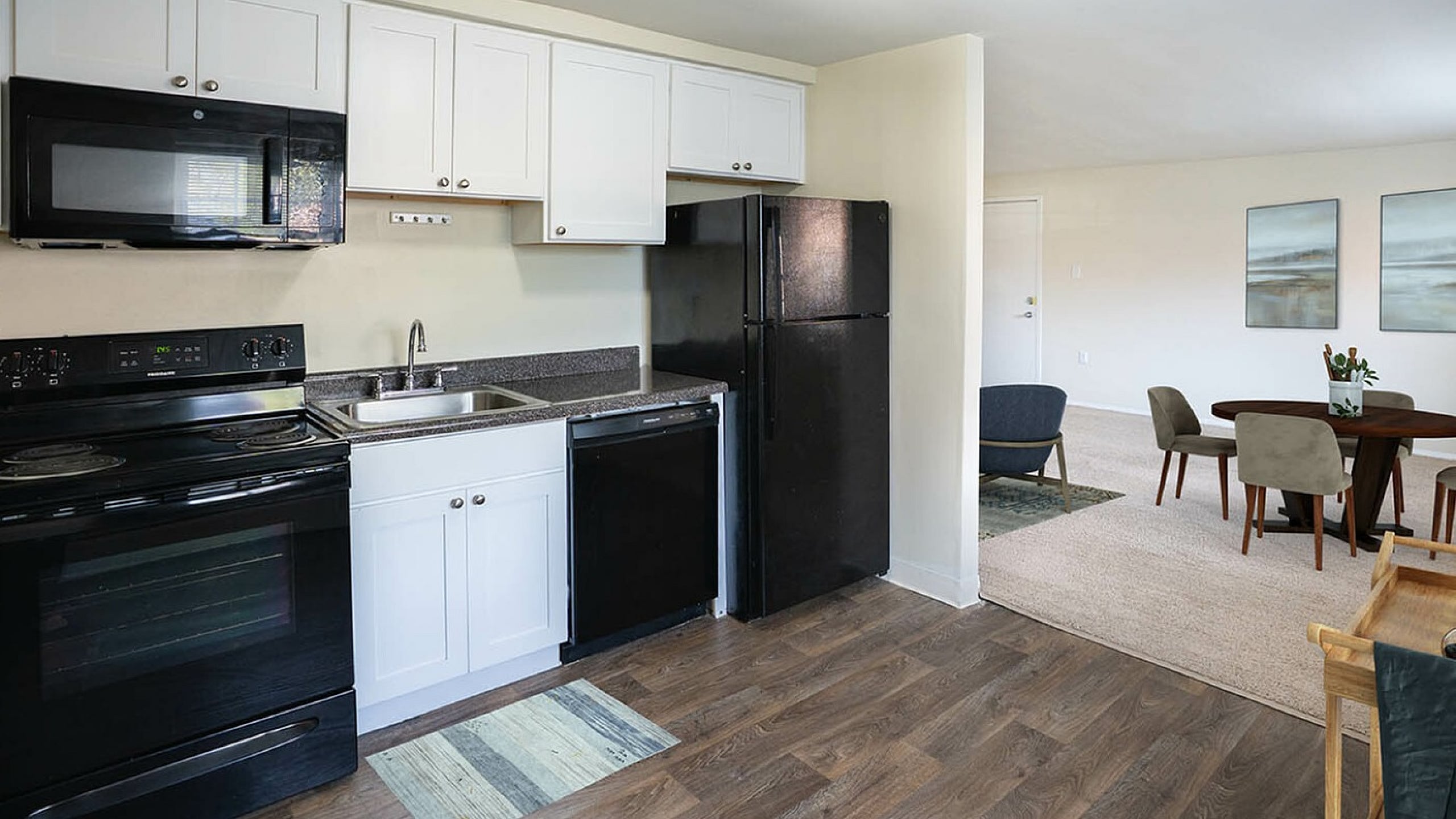 Modern kitchen with sleek black appliances and white cabinetry, adjacent to an inviting dining area with stylish decor.