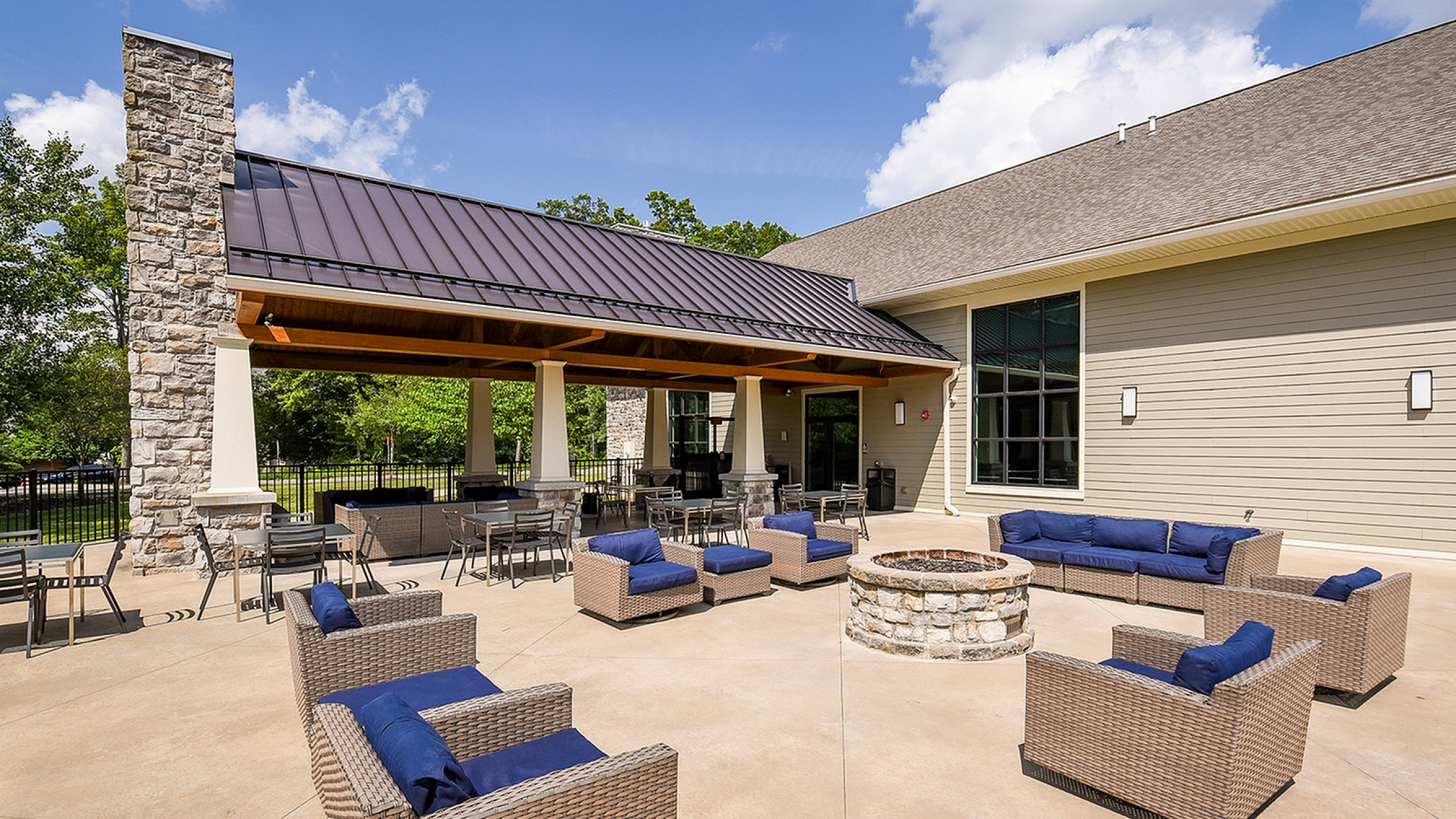 Chic outdoor patio with cozy wicker furniture and a charming stone fire pit under a modern covered gazebo, perfect for relaxation.