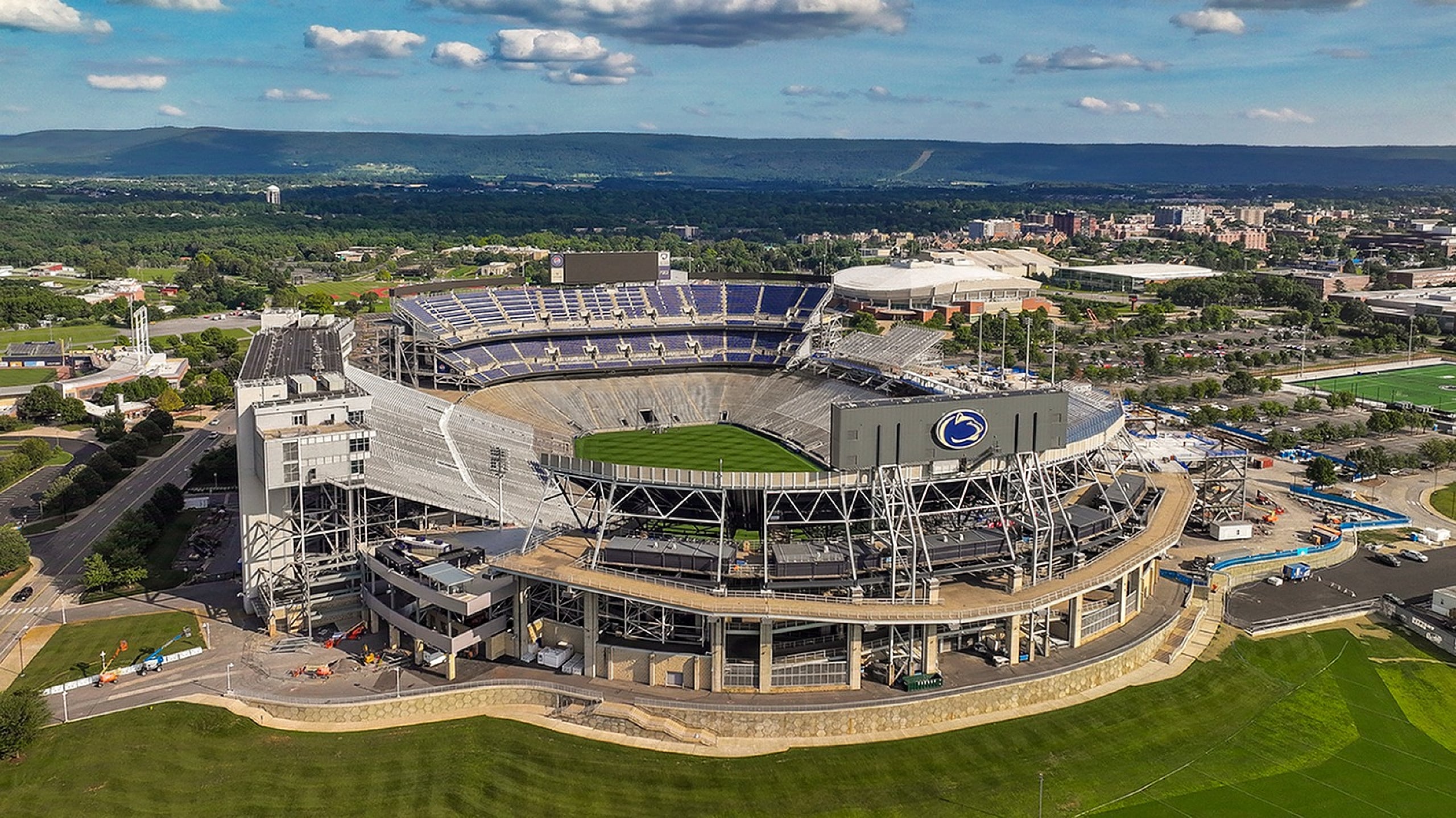 Breathtaking aerial view of a grand stadium with lush green surroundings, showcasing its impressive architecture and expansive seating.