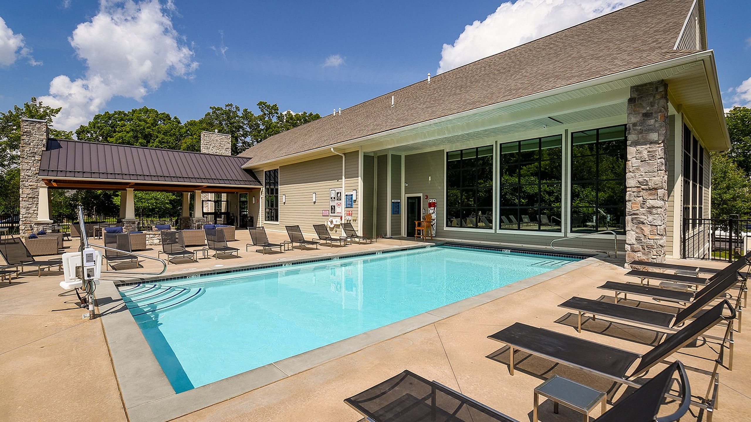 Inviting outdoor pool area with modern lounge chairs and stylish clubhouse under a bright blue sky.
