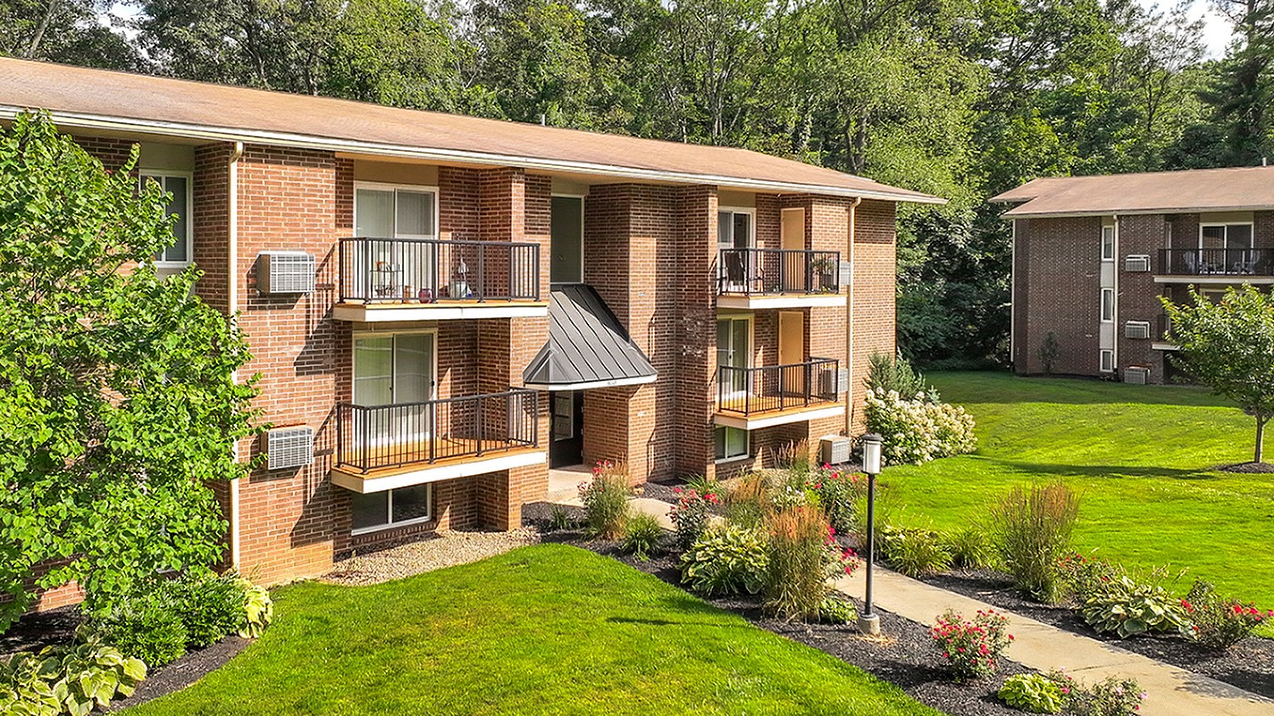 Charming brick apartment building with private balconies, nestled in lush greenery and vibrant gardens, offering a serene living environment.