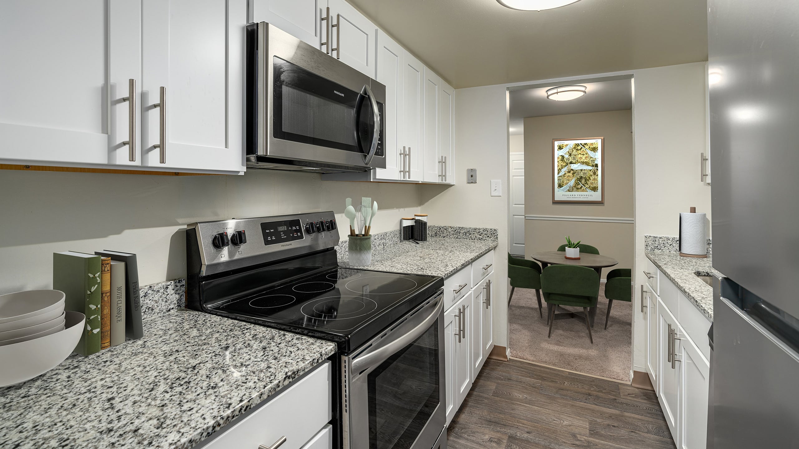 Modern kitchen with sleek stainless steel appliances, granite countertops, and elegant white cabinetry; opens into a cozy dining area with stylish green chairs.
