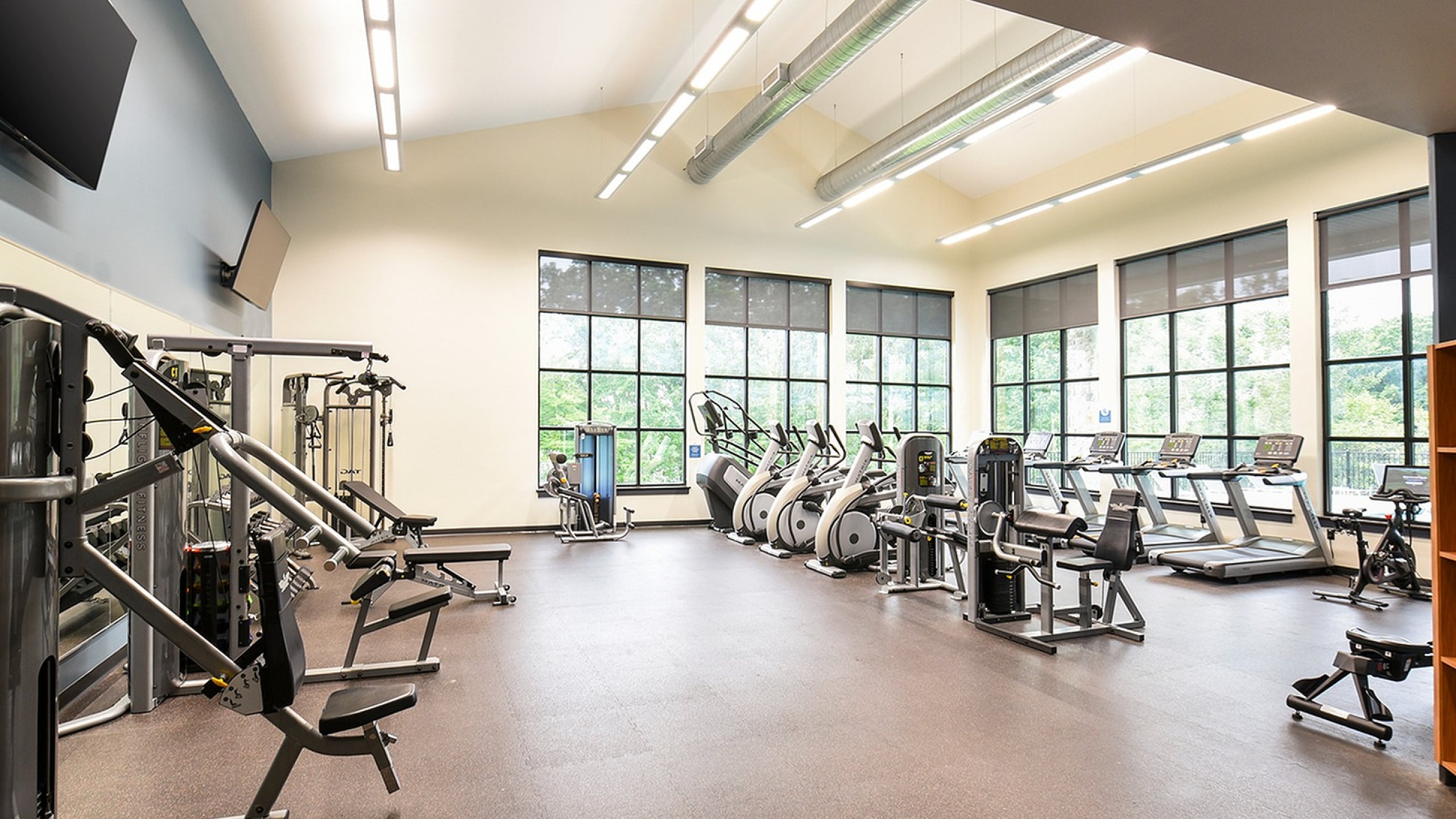Modern fitness center with state-of-the-art equipment, bright natural lighting, and expansive windows offering scenic views.