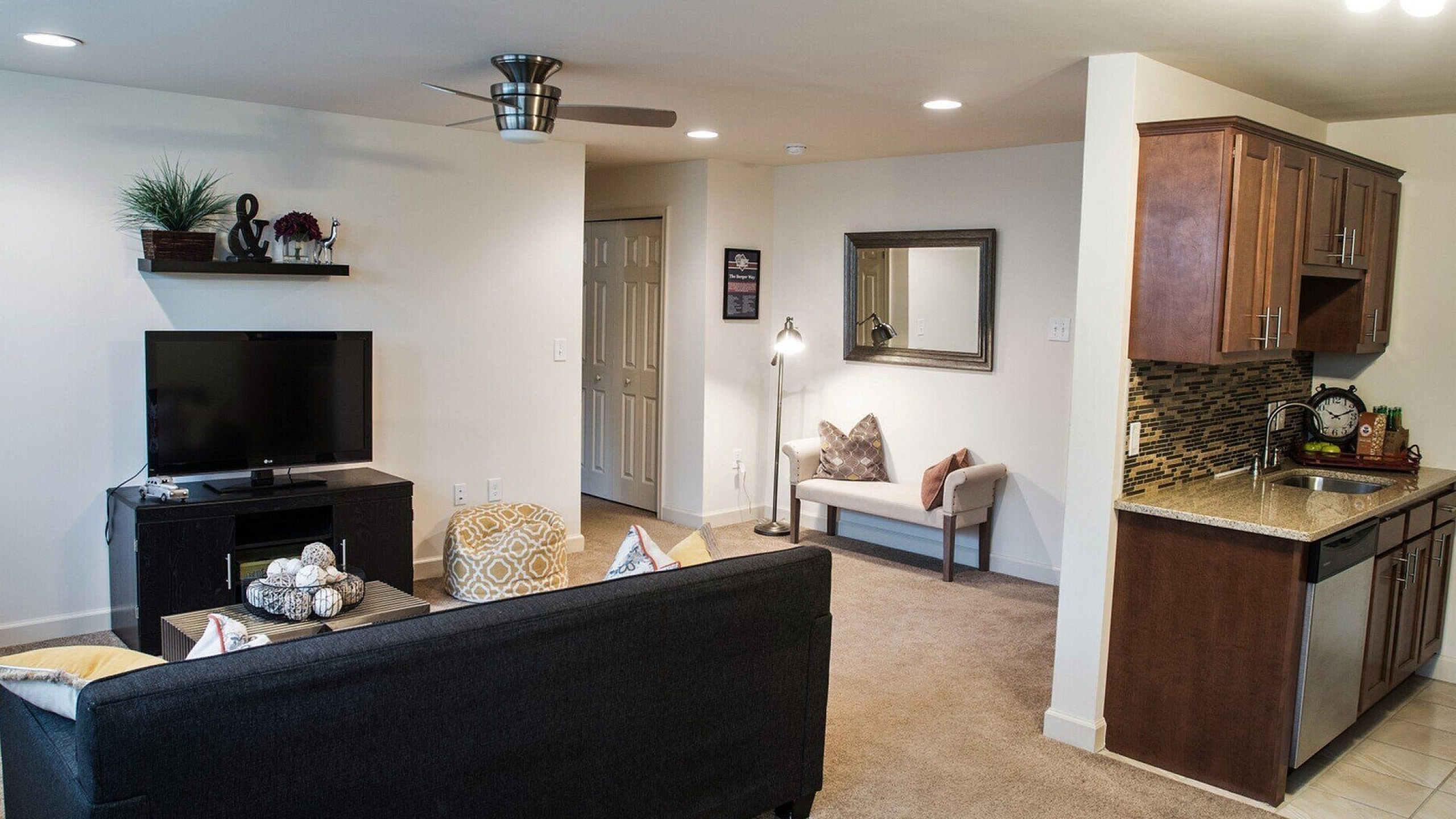 Modern apartment living room with cozy seating, stylish wall decor, open concept kitchen, and warm lighting.