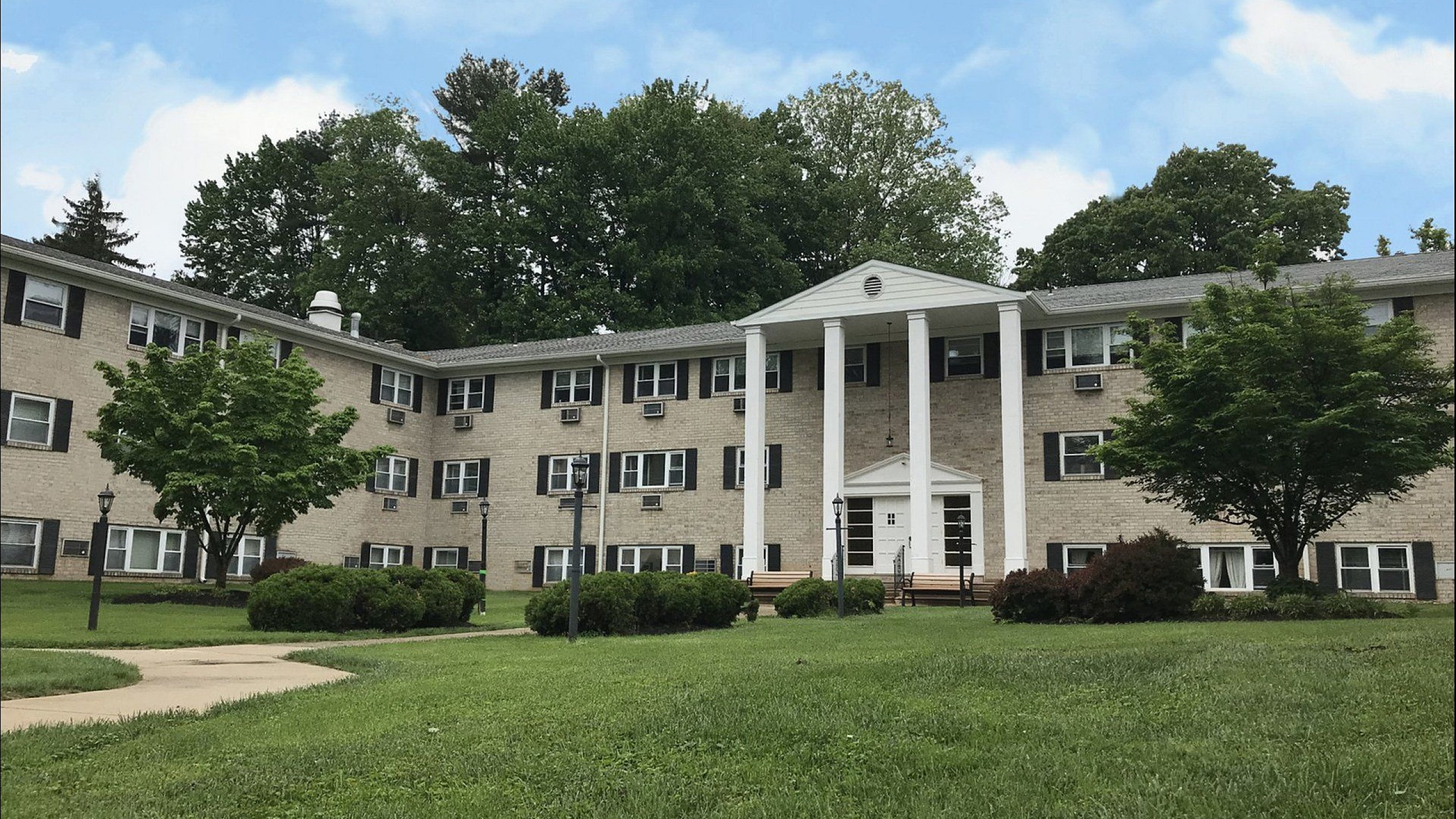 Inviting apartment building with charming colonial architecture set amidst lush greenery and a tranquil environment.