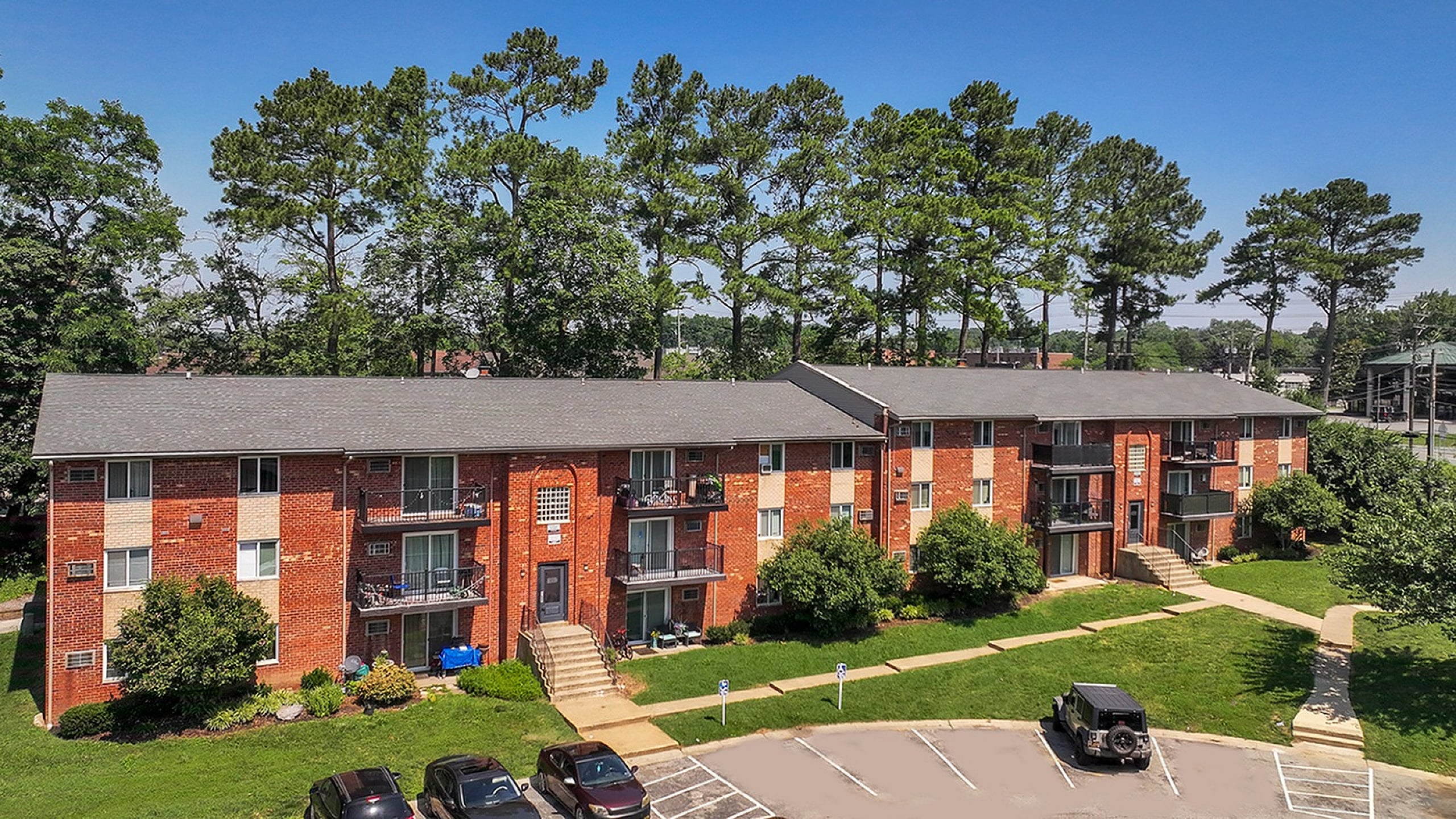 Charming brick apartment complex nestled among tall, lush trees with convenient parking and attractive landscaping.