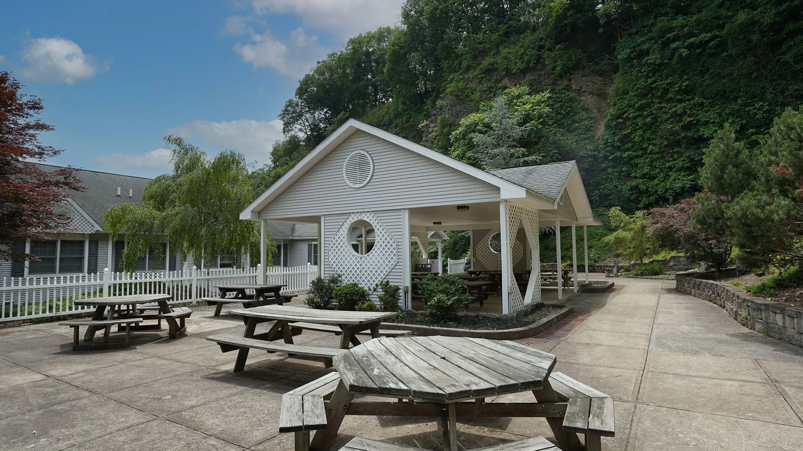 Charming outdoor communal area with wooden picnic tables and a stylish pavilion, surrounded by lush greenery for a peaceful retreat.