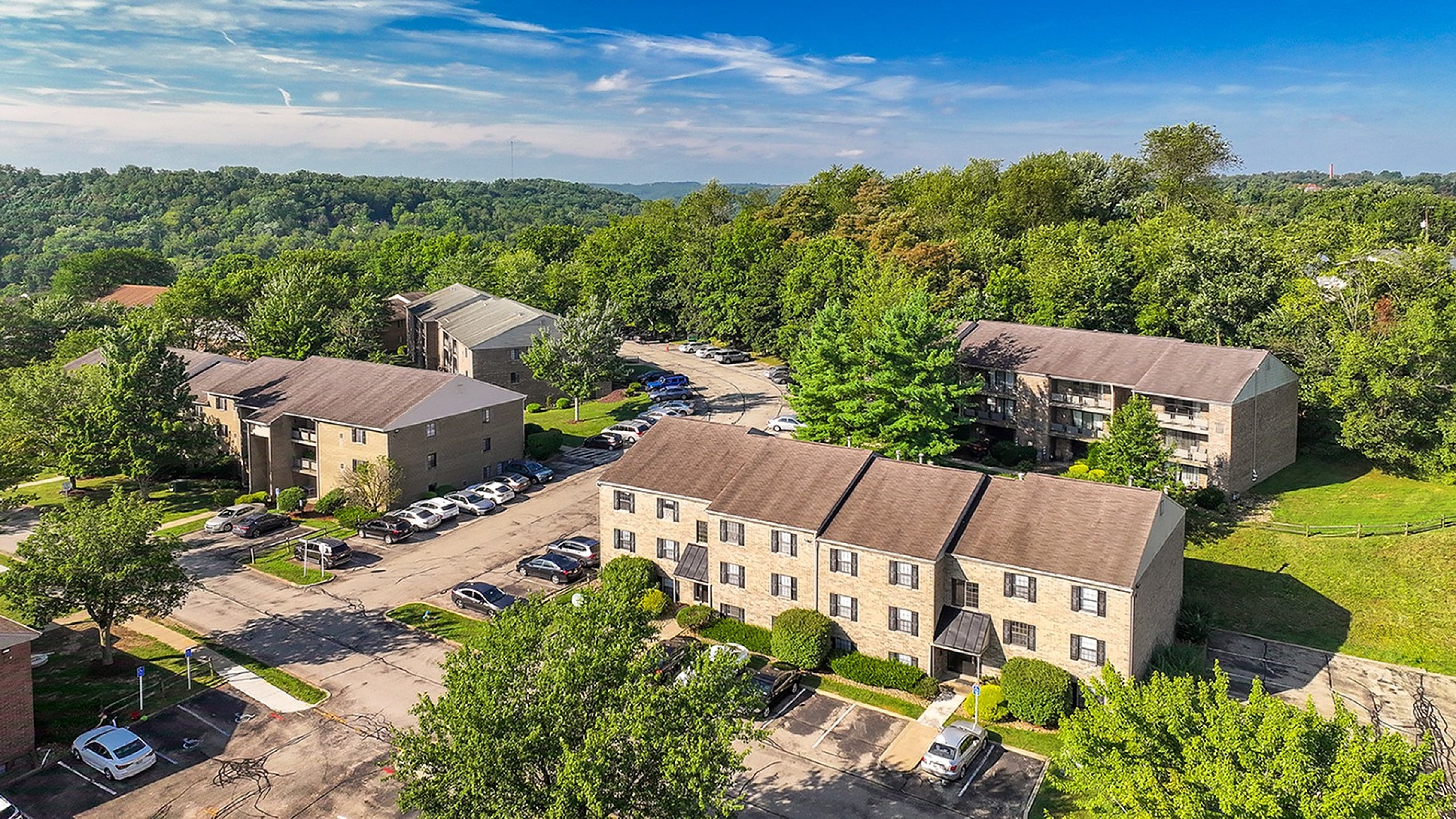Charming apartment complex surrounded by lush greenery, featuring ample parking and scenic views under a vibrant blue sky.