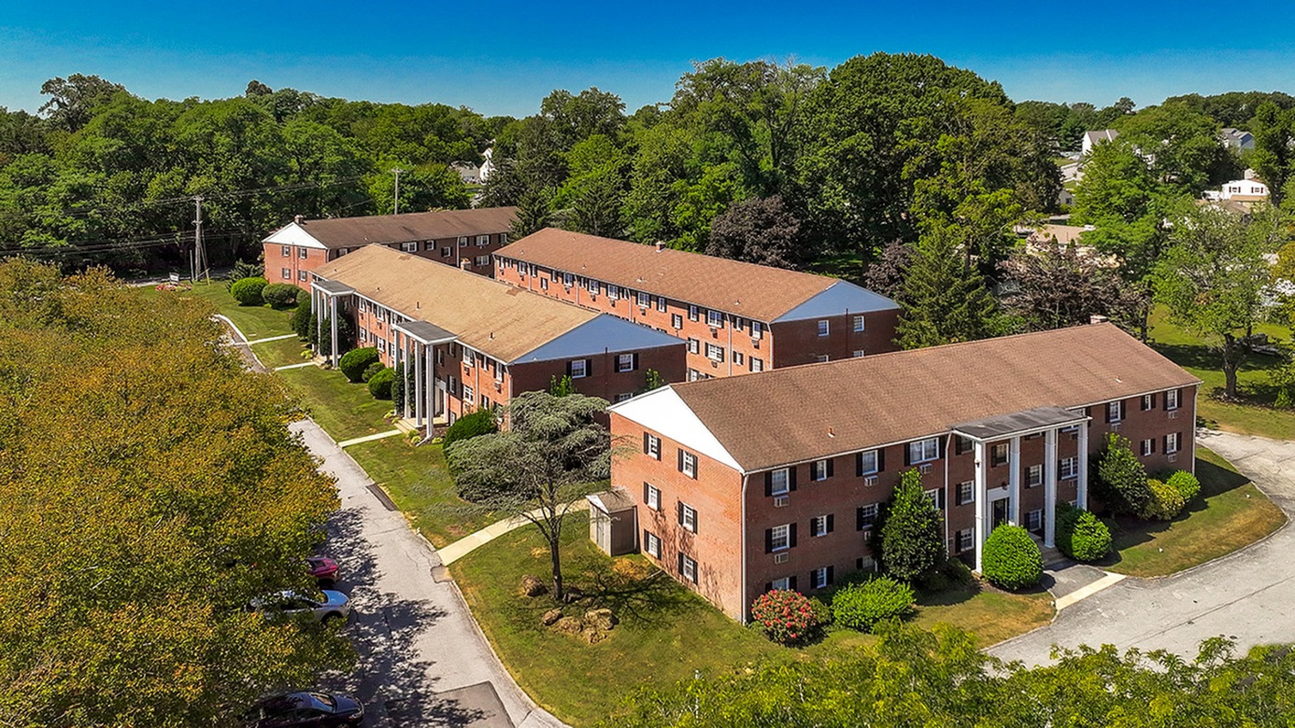 Charming brick apartment complex surrounded by lush greenery, featuring classic architectural design and ample parking space.