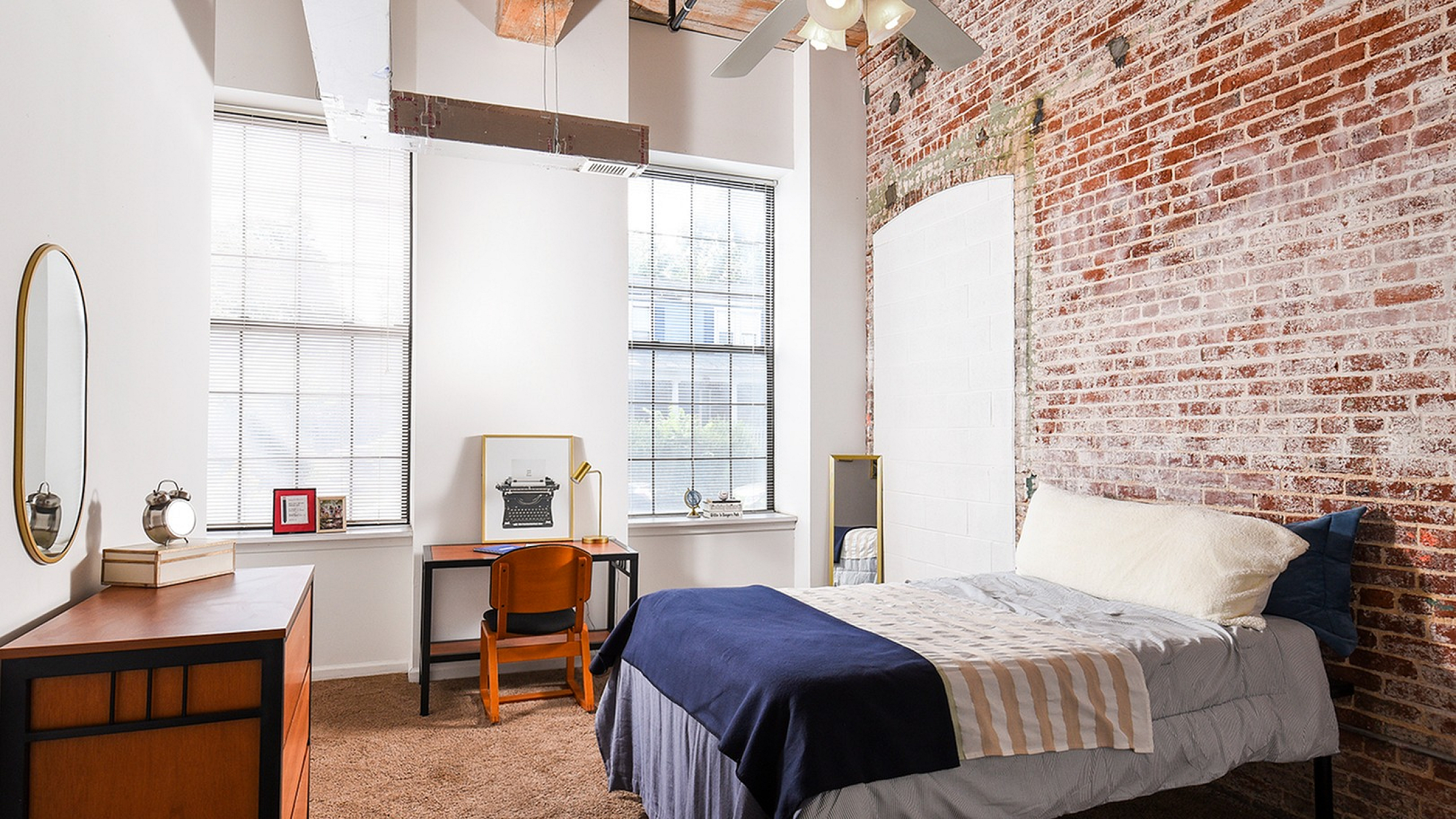 Charming loft bedroom with exposed brick walls, large windows, and a cozy workspace for creative inspiration.