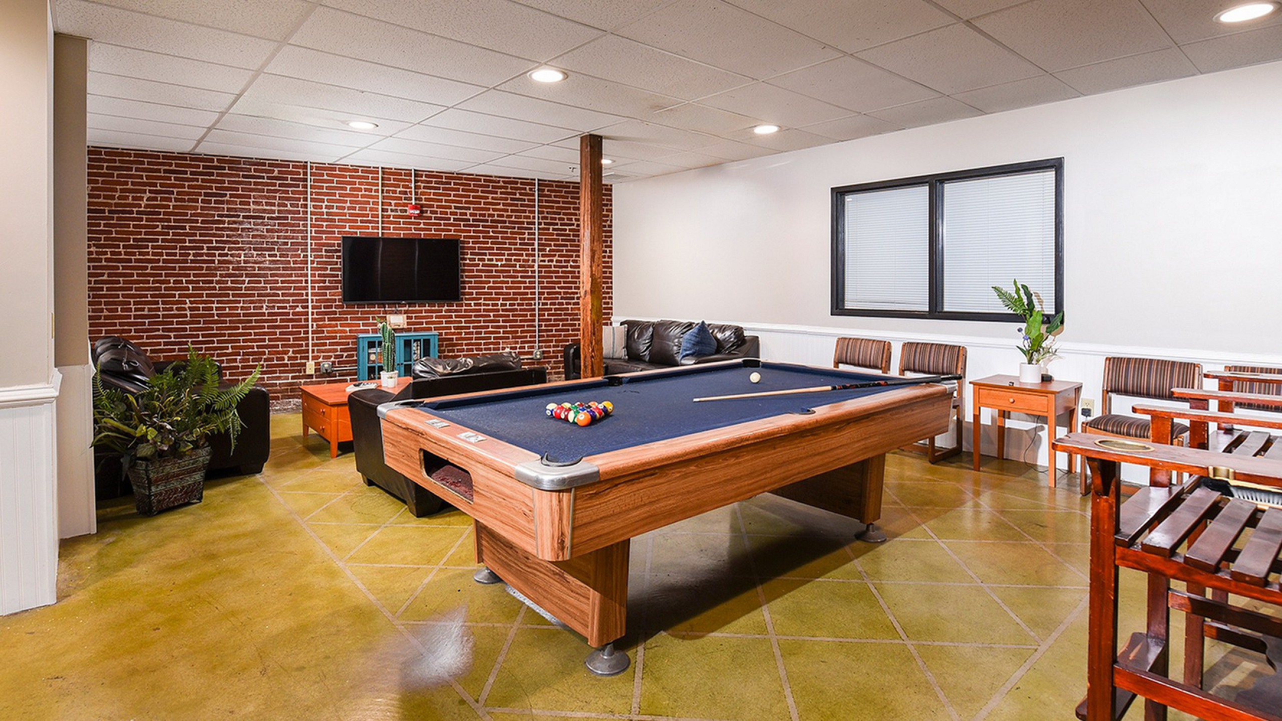 Chic recreation room with a pool table, cozy seating area, and vibrant brick accent wall, perfect for entertaining.