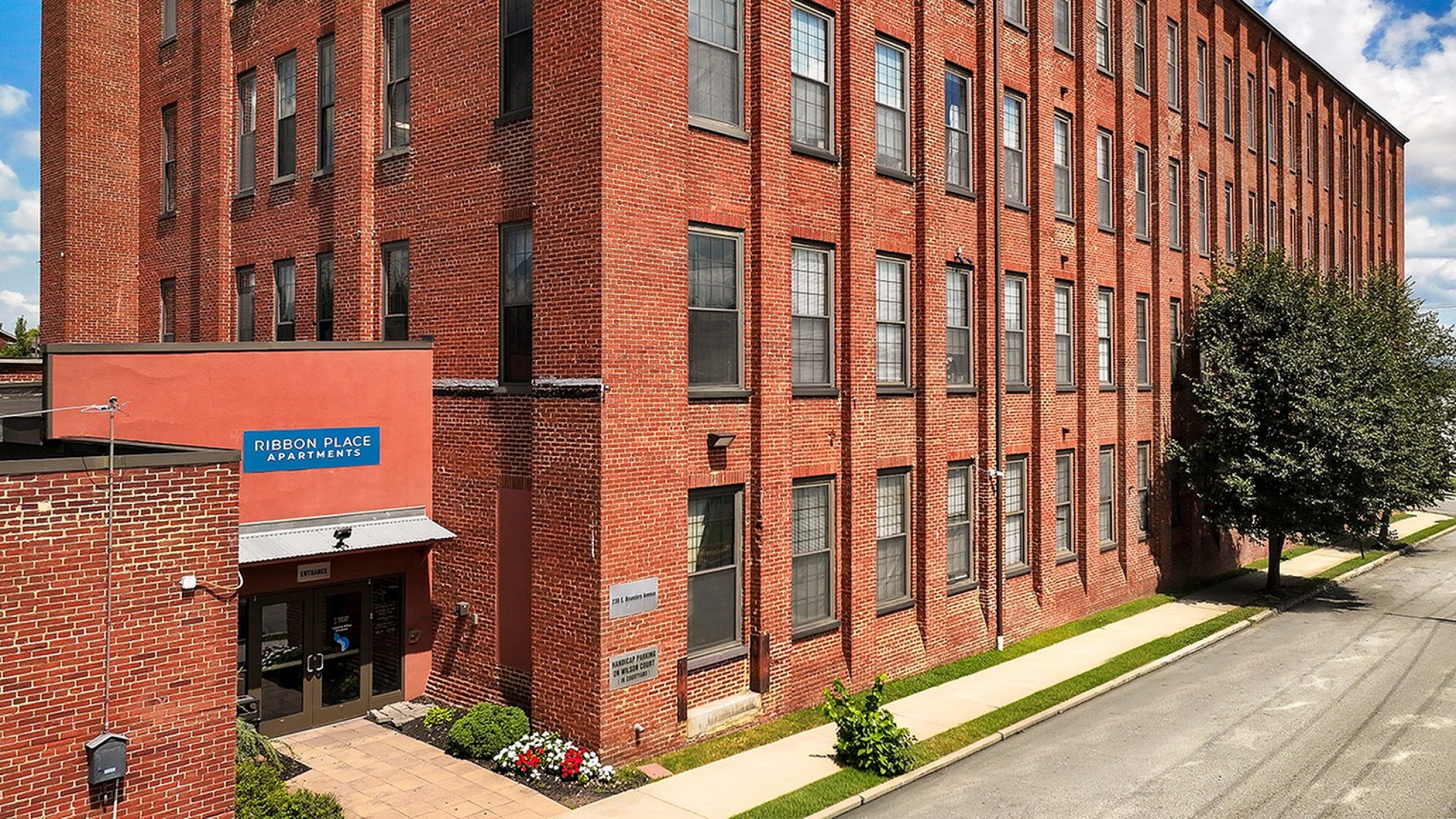 Charming brick exterior of Ribbon Place Apartments with lush landscaping, showcasing a blend of historic architecture and modern living.