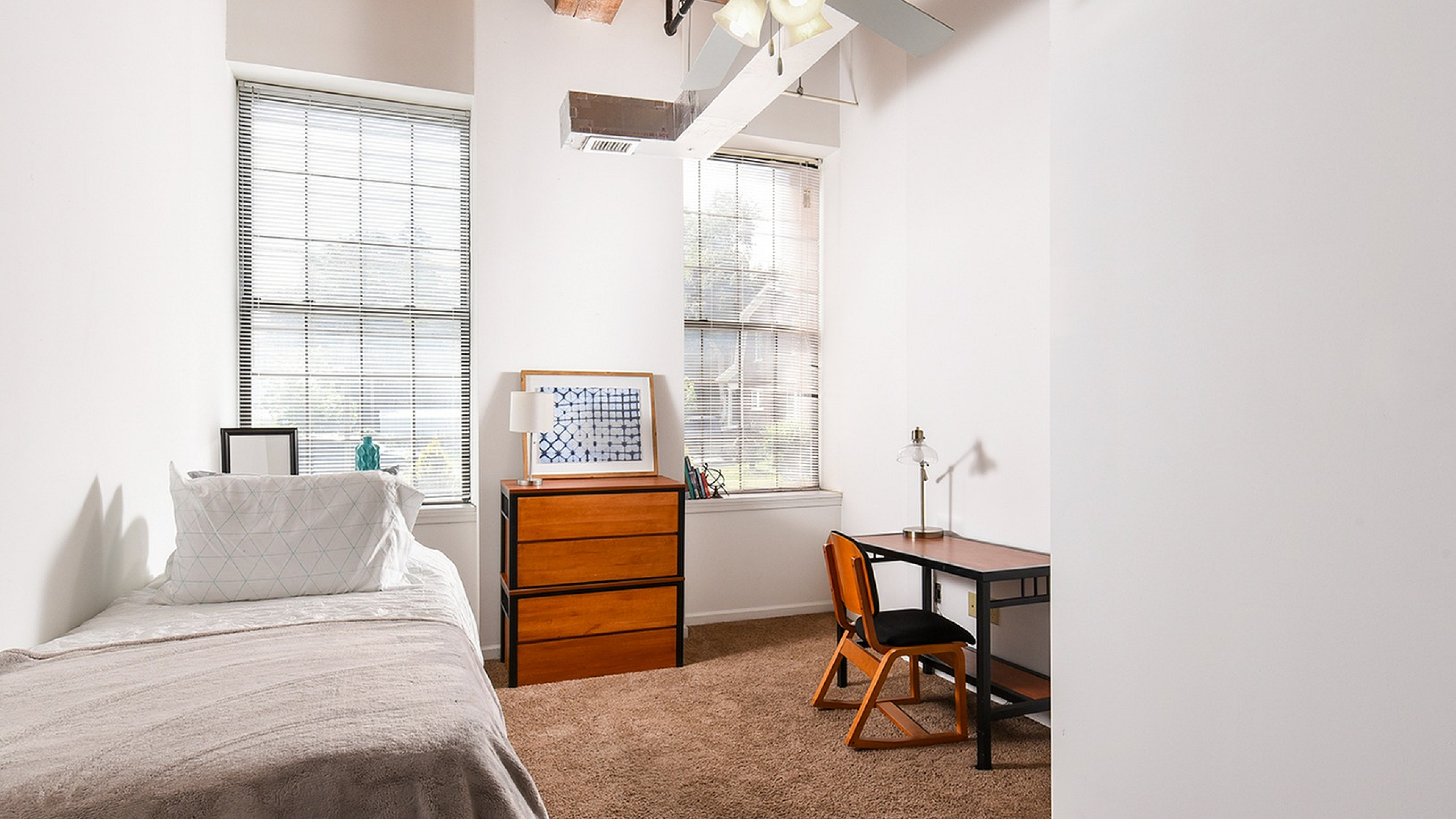 Cozy bedroom with a modern design featuring large windows, a stylish desk, and a comfortable bed. Wooden furniture adds warmth and sophistication.