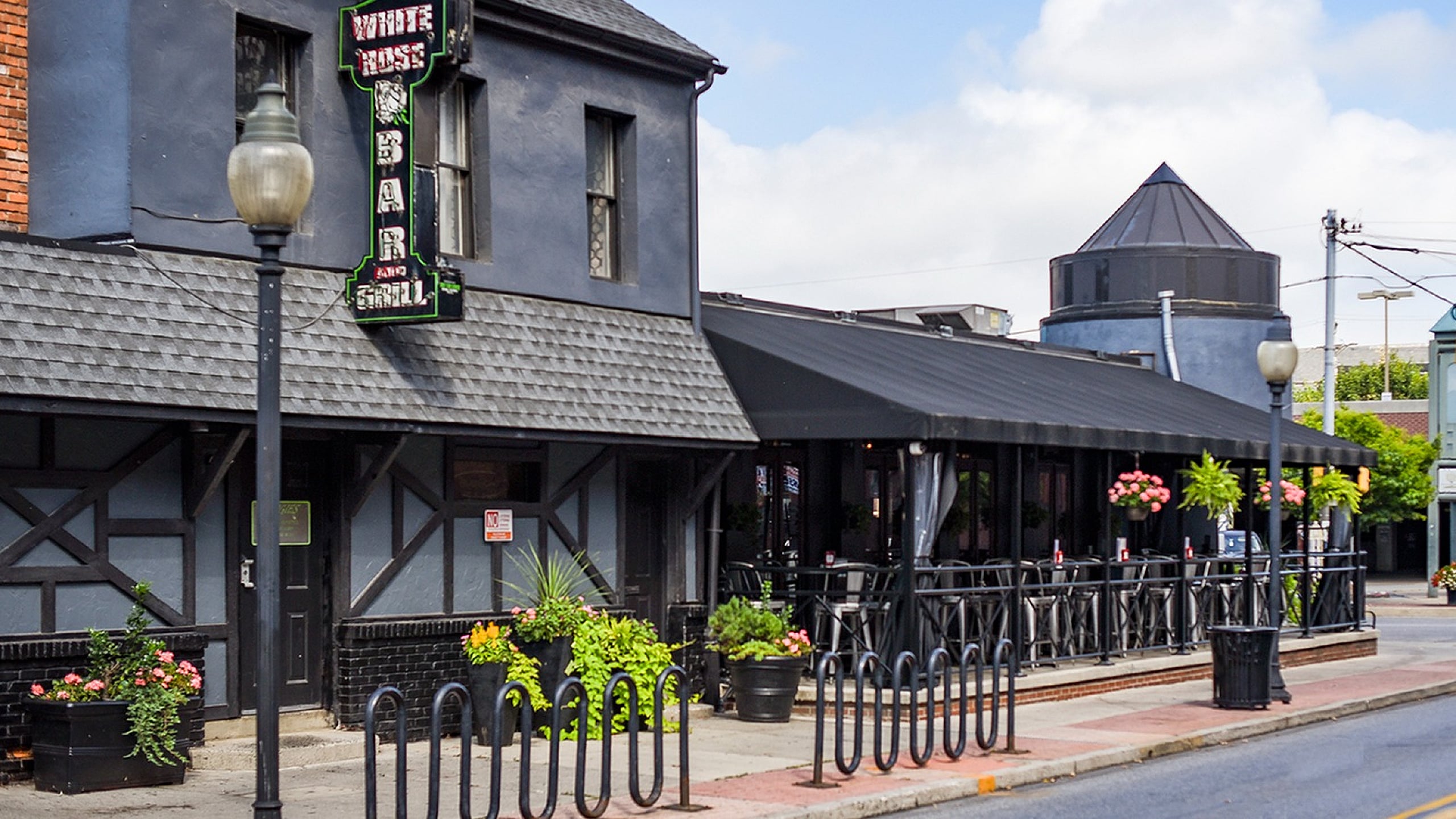 Charming street view of a quaint bar and grill with a stylish exterior, adorned with vibrant flower pots and inviting outdoor seating.