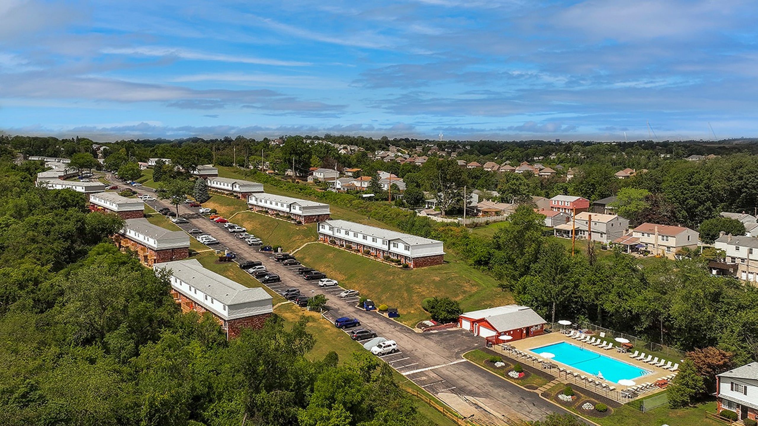 Scenic aerial view of a charming hillside apartment community with refreshing swimming pool, surrounded by lush greenery and vibrant neighborhood.
