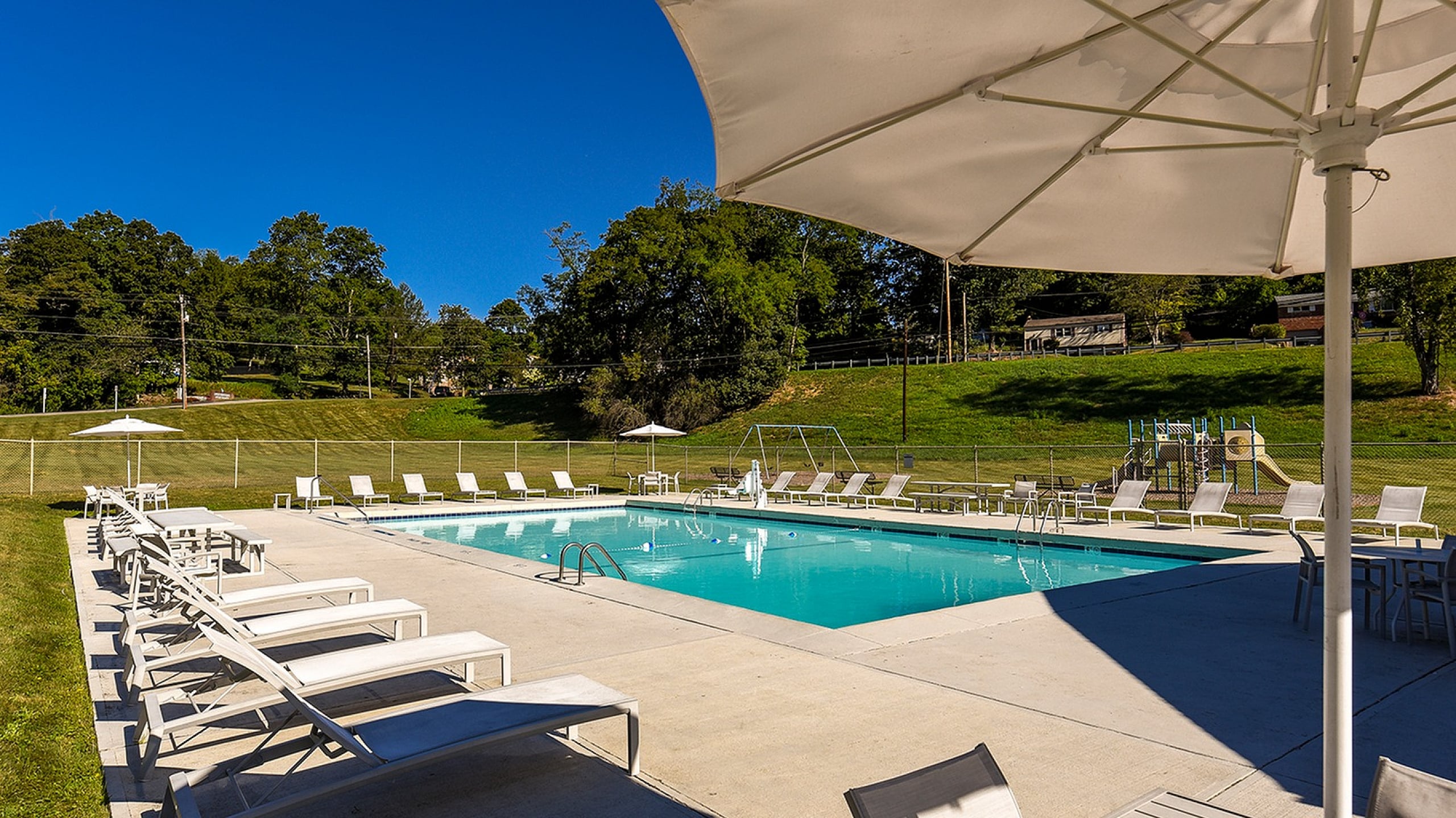 Inviting outdoor swimming pool surrounded by stylish white loungers and sun umbrellas, set against a serene backdrop of lush greenery.