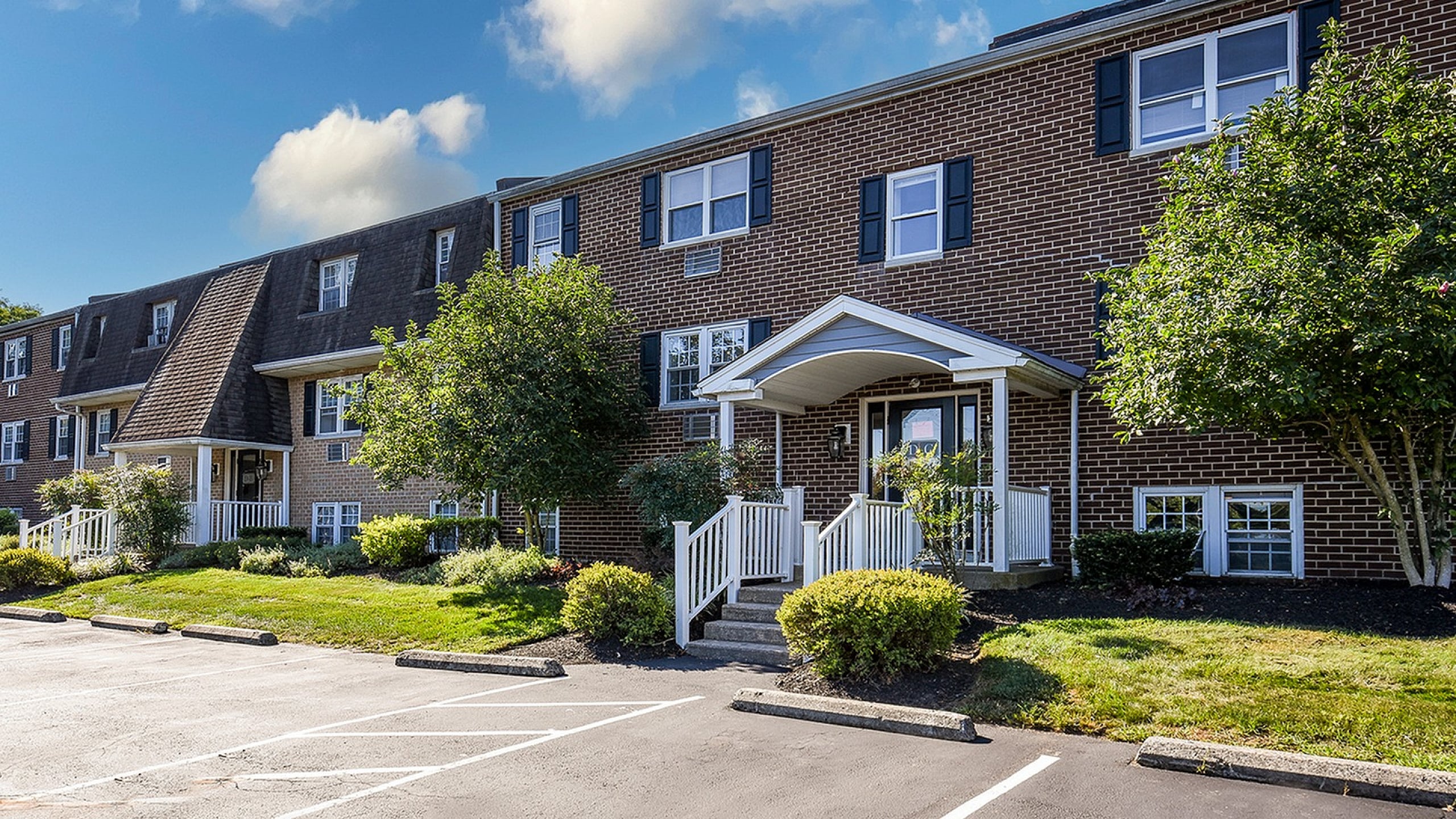 Charming brick apartment buildings with classic architectural design, nestled in a lush, landscaped setting under a clear blue sky.