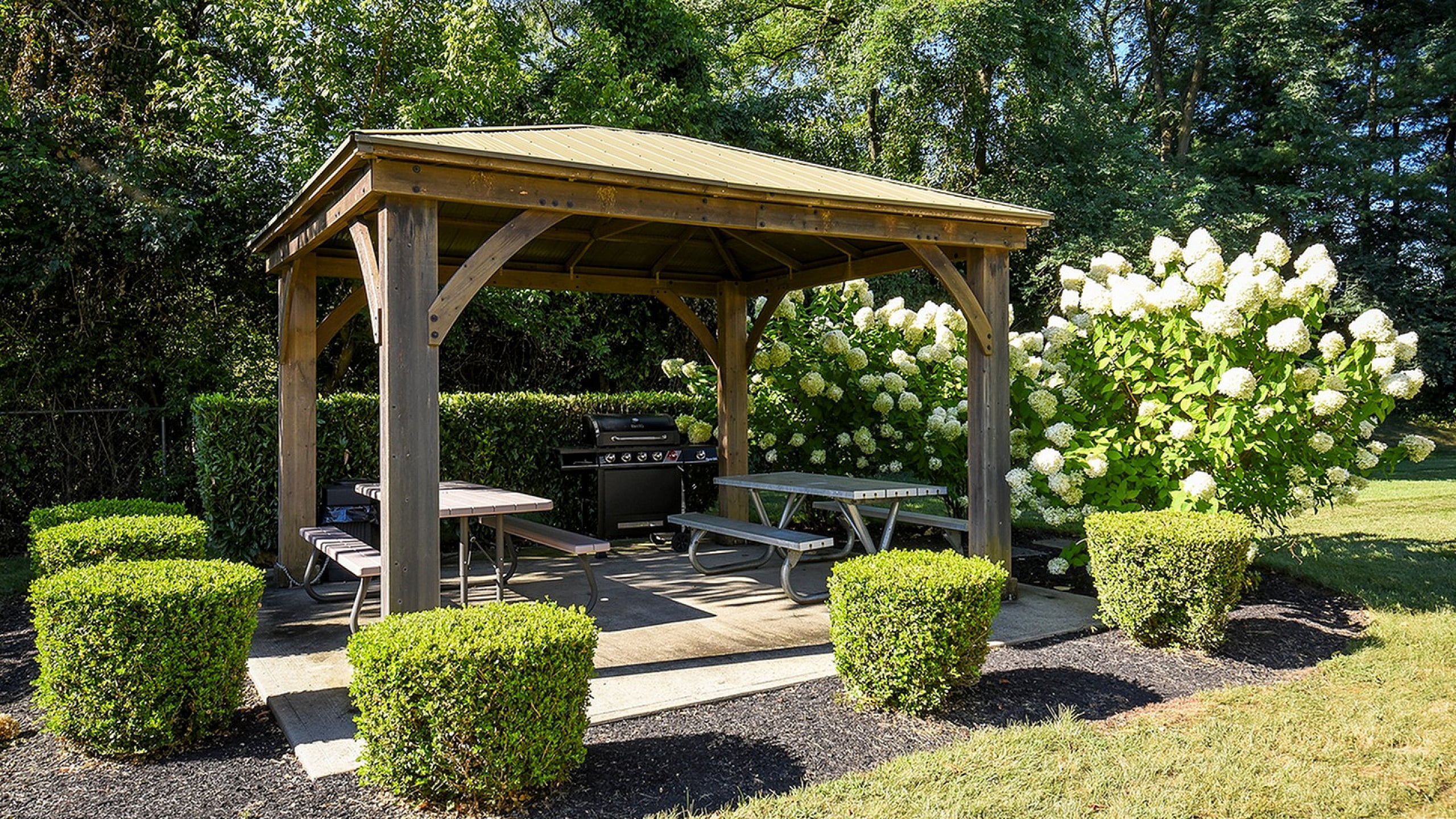 Charming garden gazebo with picnic tables, surrounded by lush greenery and blooming hydrangeas, perfect for outdoor gatherings.