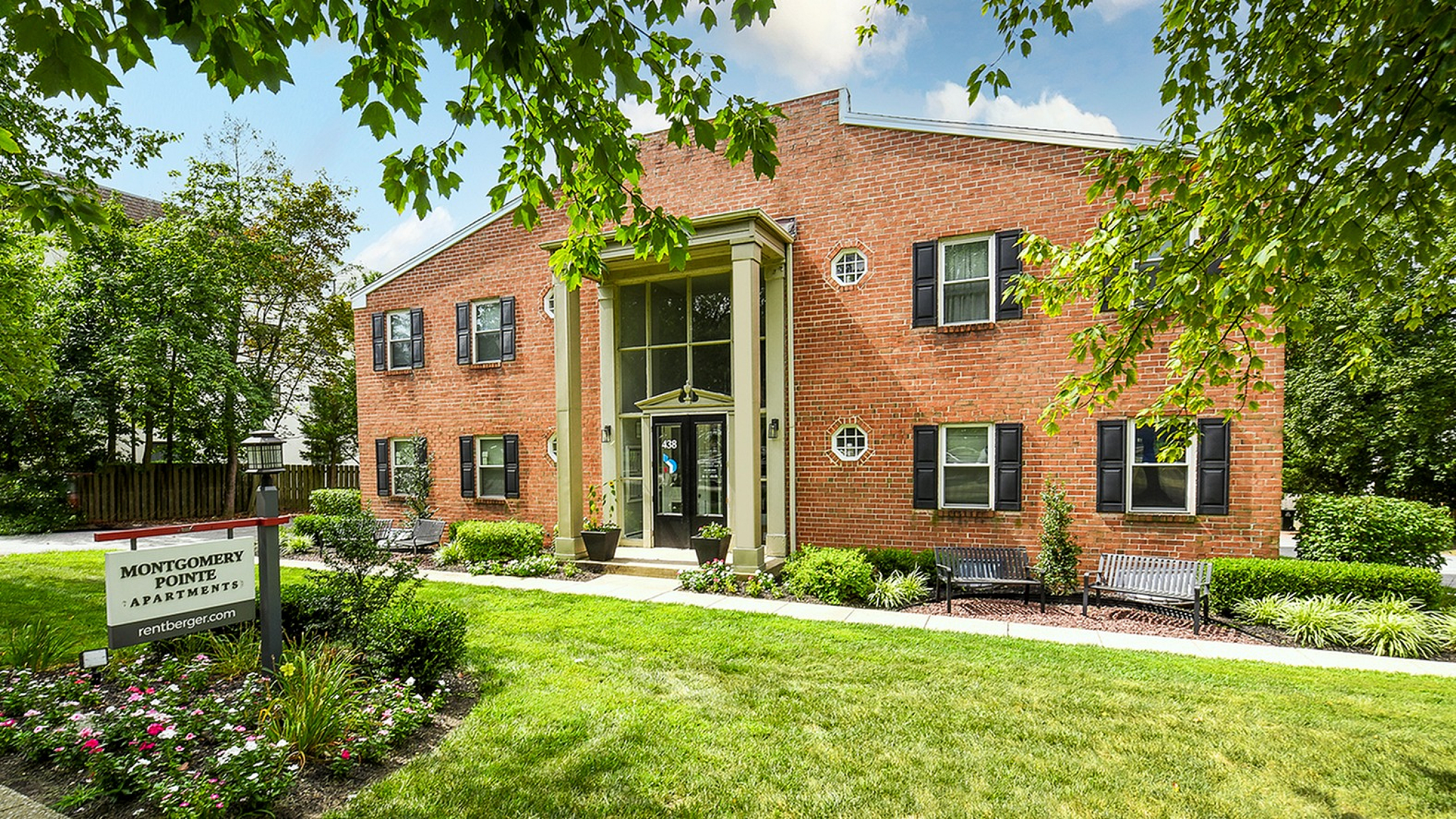 Charming red brick apartment building surrounded by lush greenery, with elegant entryway and inviting curb appeal at Montgomery Pointe Apartments.