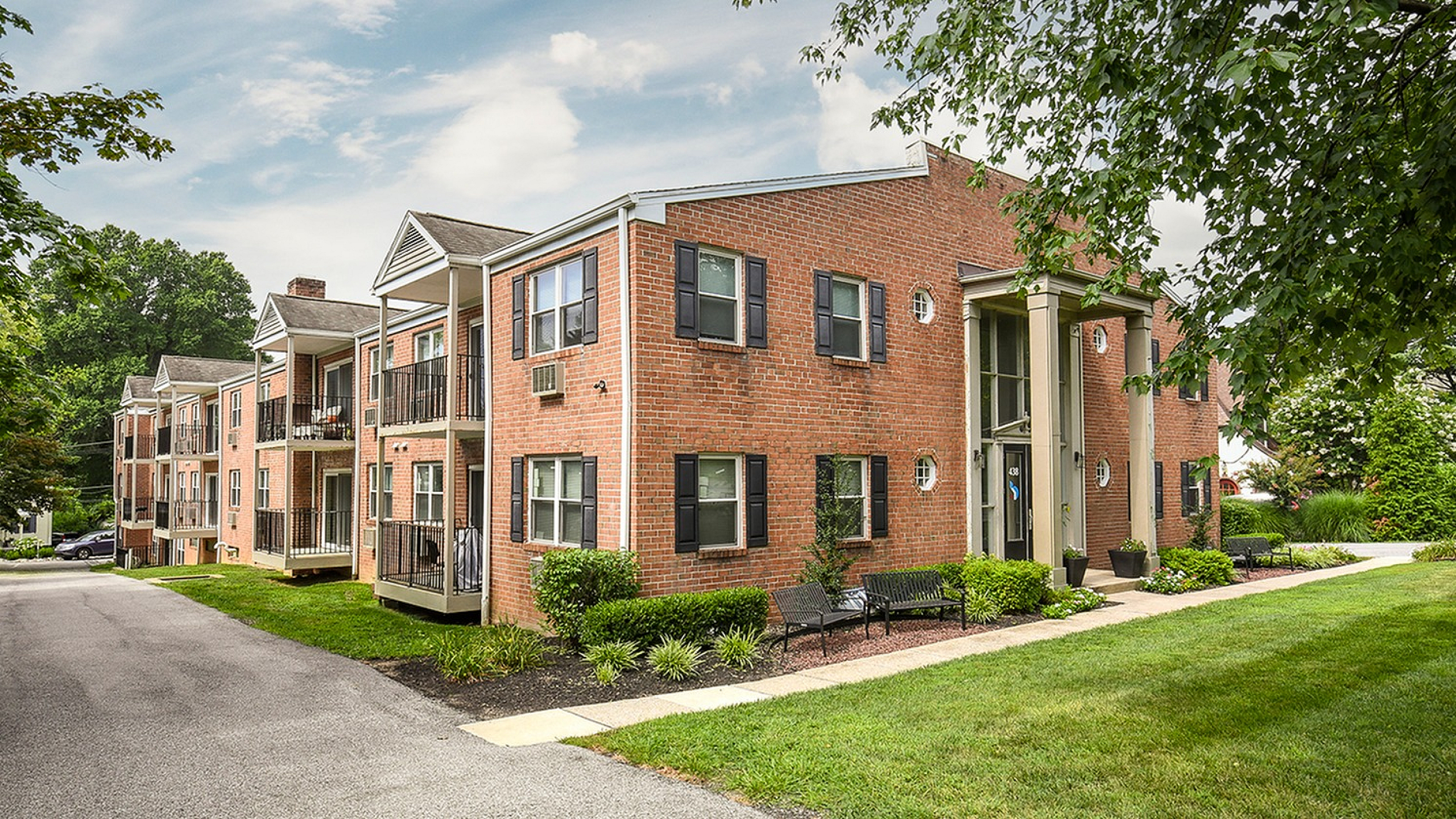 Charming brick apartment building with balconies, nestled in lush greenery, offering serene living spaces.