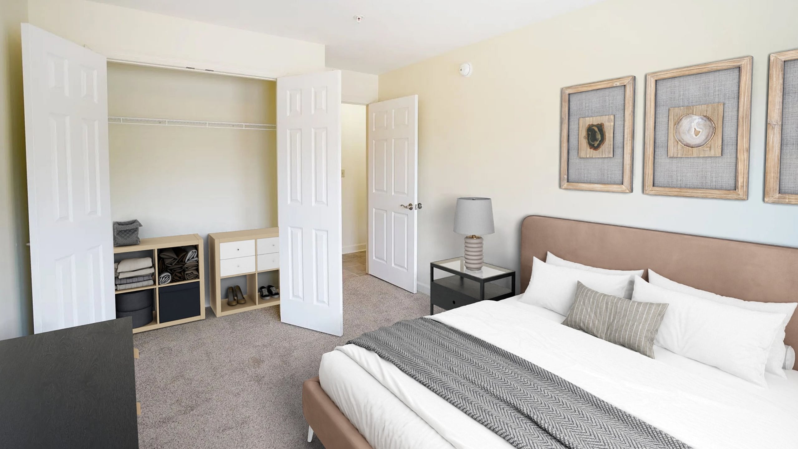 Elegant bedroom featuring plush carpeting, a cozy bed with stylish artwork, ample closet space, and modern lighting.