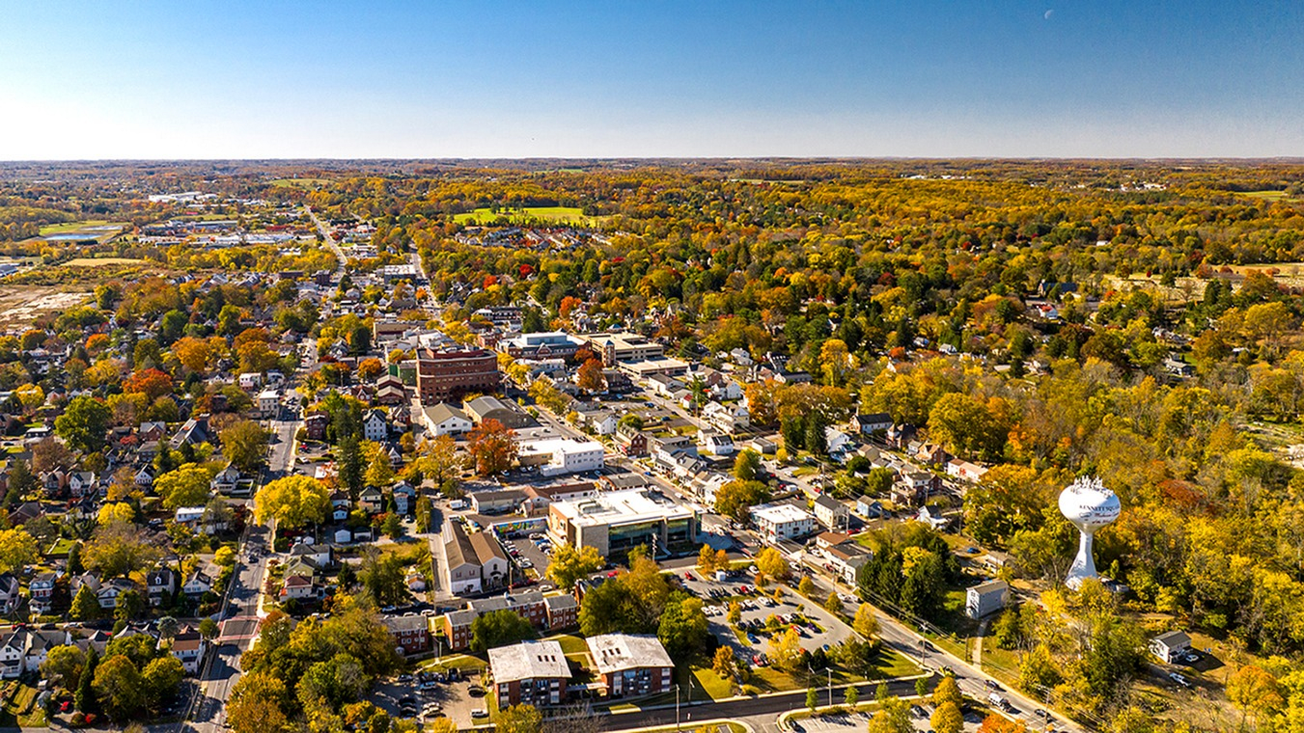 Vibrant aerial view of a charming town bathed in autumn hues, showcasing a mix of residential and commercial areas surrounded by lush greenery and scenic landscapes.